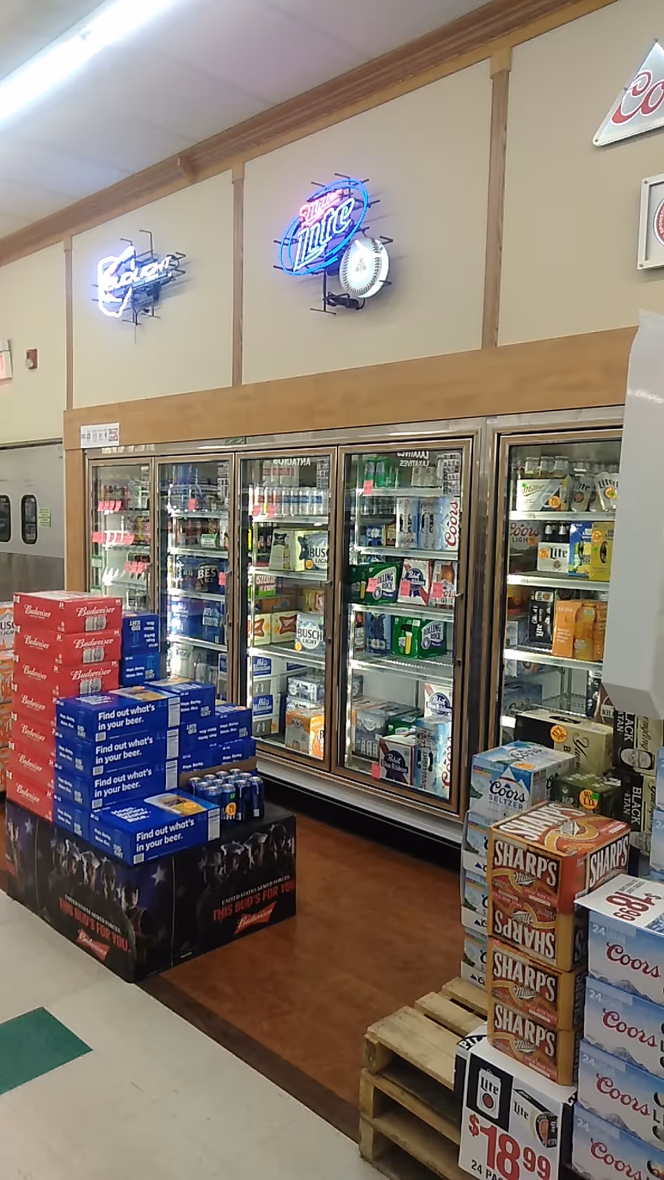 Inside Discount Drug Mart, a refrigerated beverage display with beer cases and pallets.