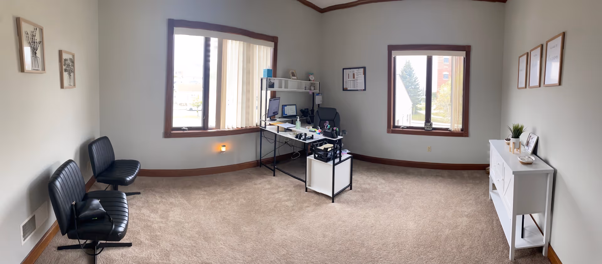 Senior care facility office: desk with computer, two black chairs, windows, and a white cabinet.