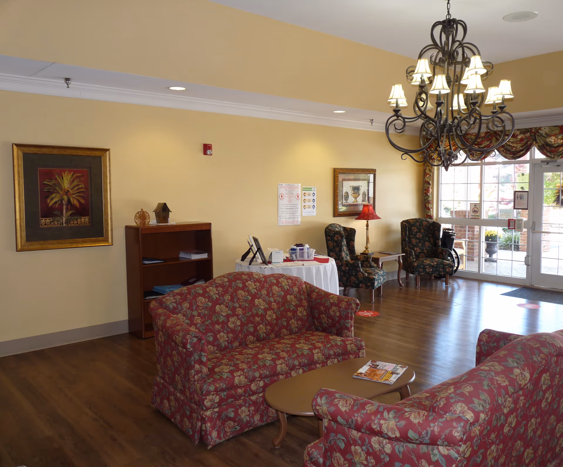 Cozy lobby with floral sofas, round tables, and a chandelier in a retirement center.