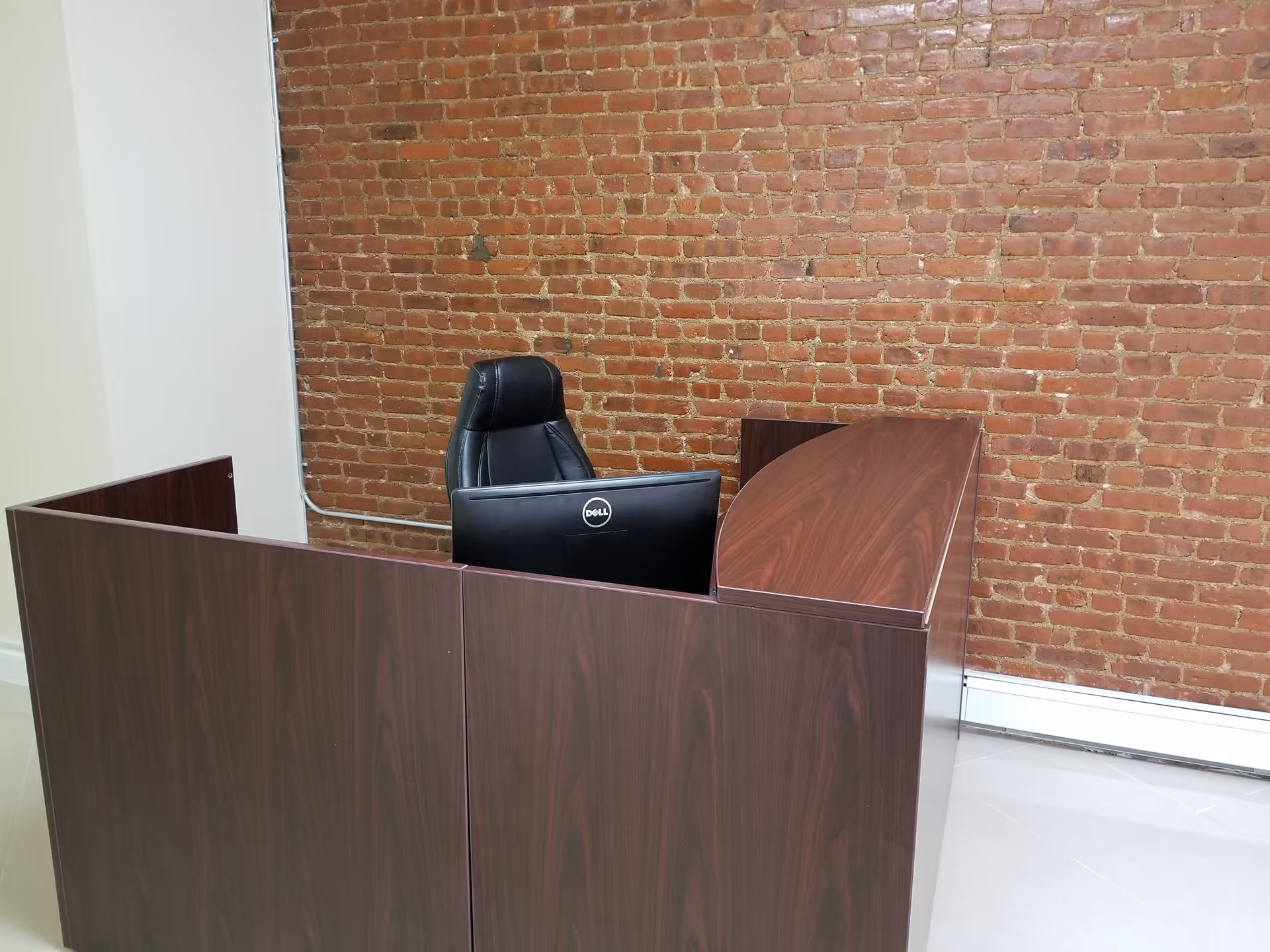 Reception desk with dark wood, black chair, and brick wall backdrop inside facility.