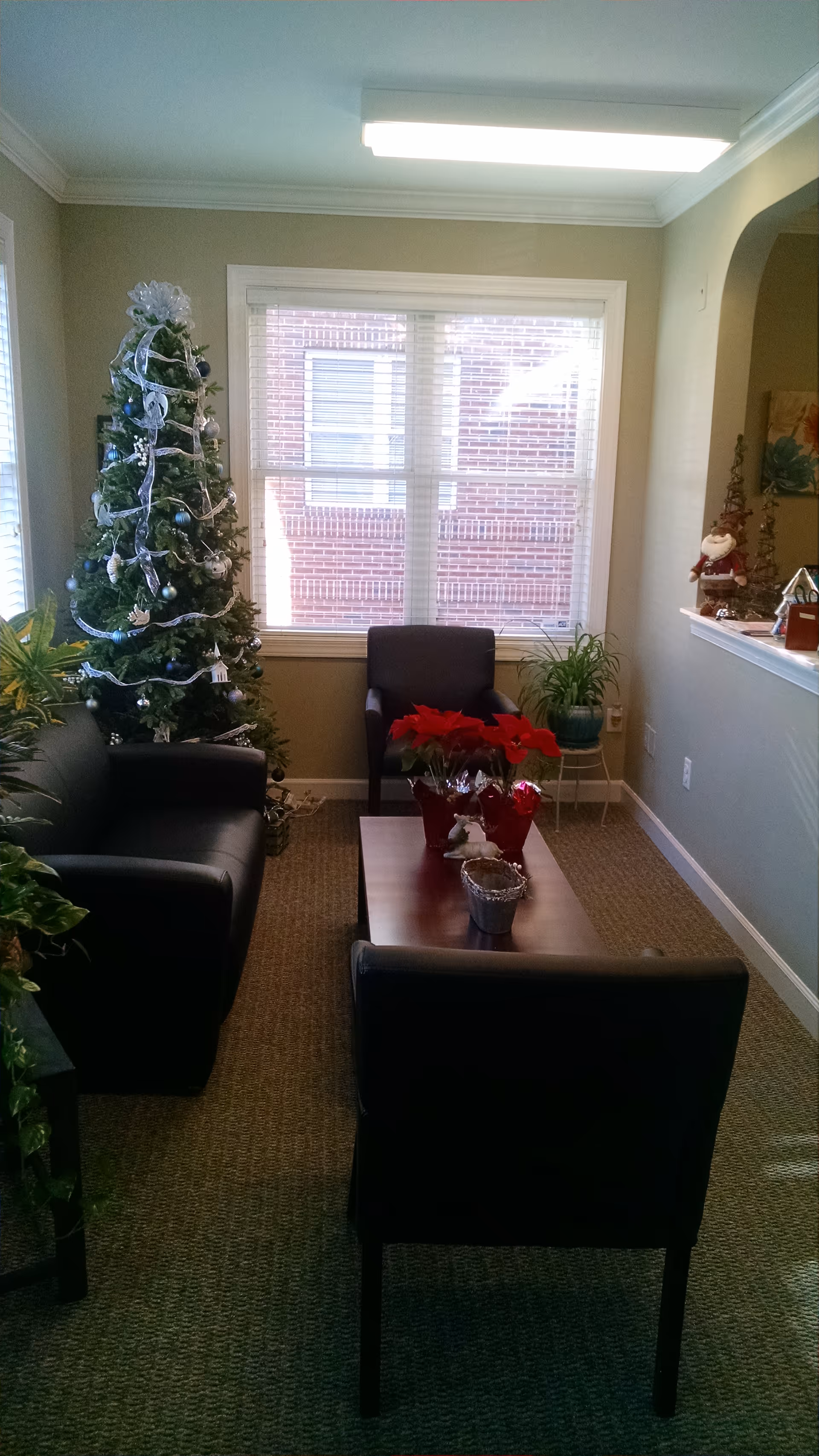 Cozy interior lounge with a Christmas tree, plants, and black leather chairs around a coffee table.