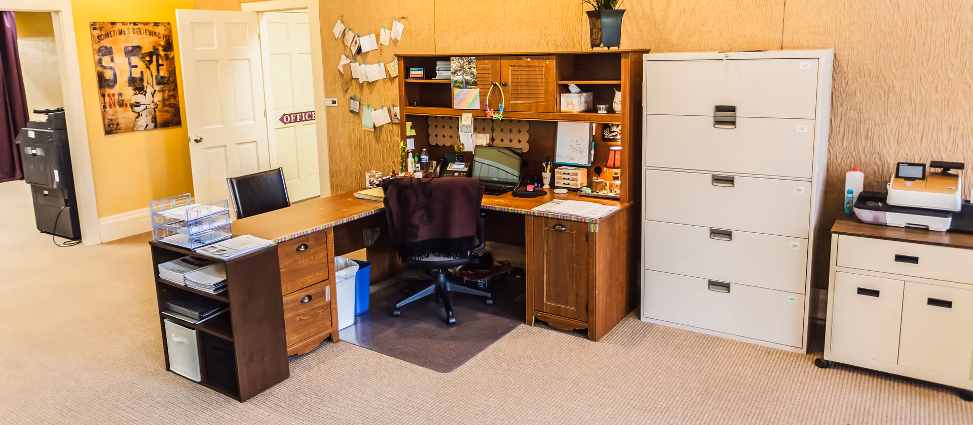 Administrative desk area with chair, filing cabinets, and shelves in a senior facility.