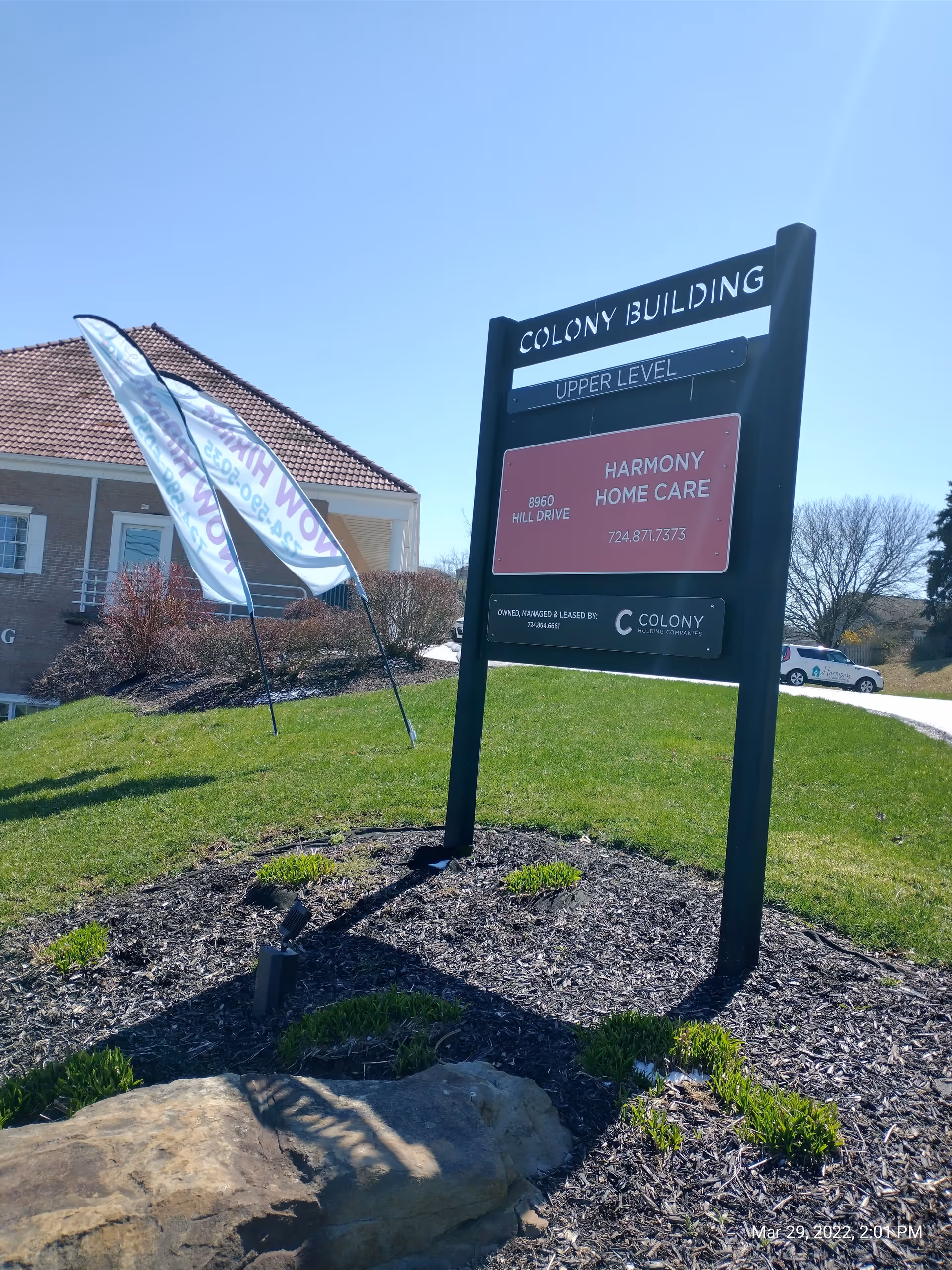 Outdoor scene featuring a Colony Building sign for Harmony Home Care with flag banners nearby.