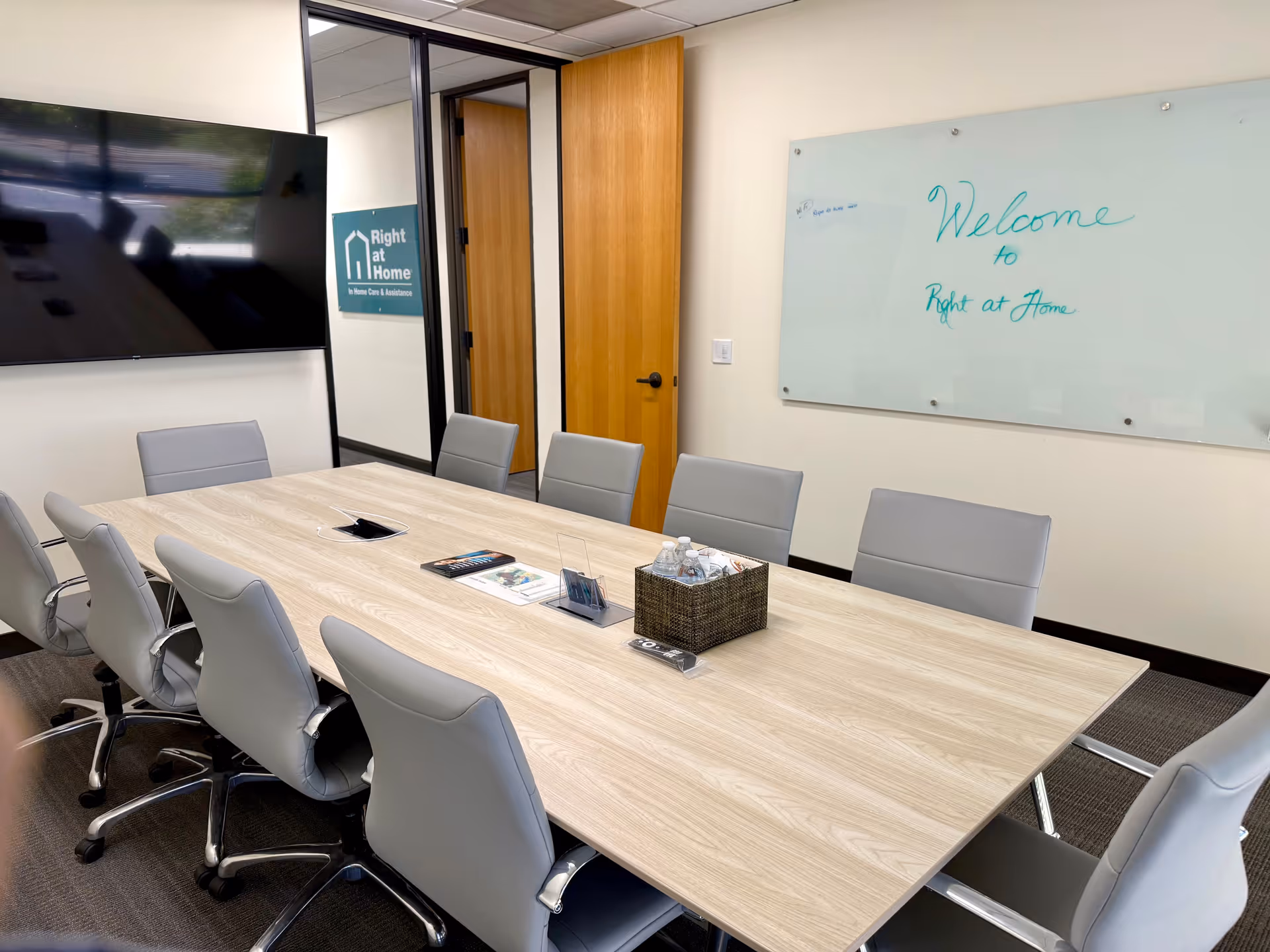 Right at Home conference room featuring a long table, gray chairs, TV, and whiteboard.