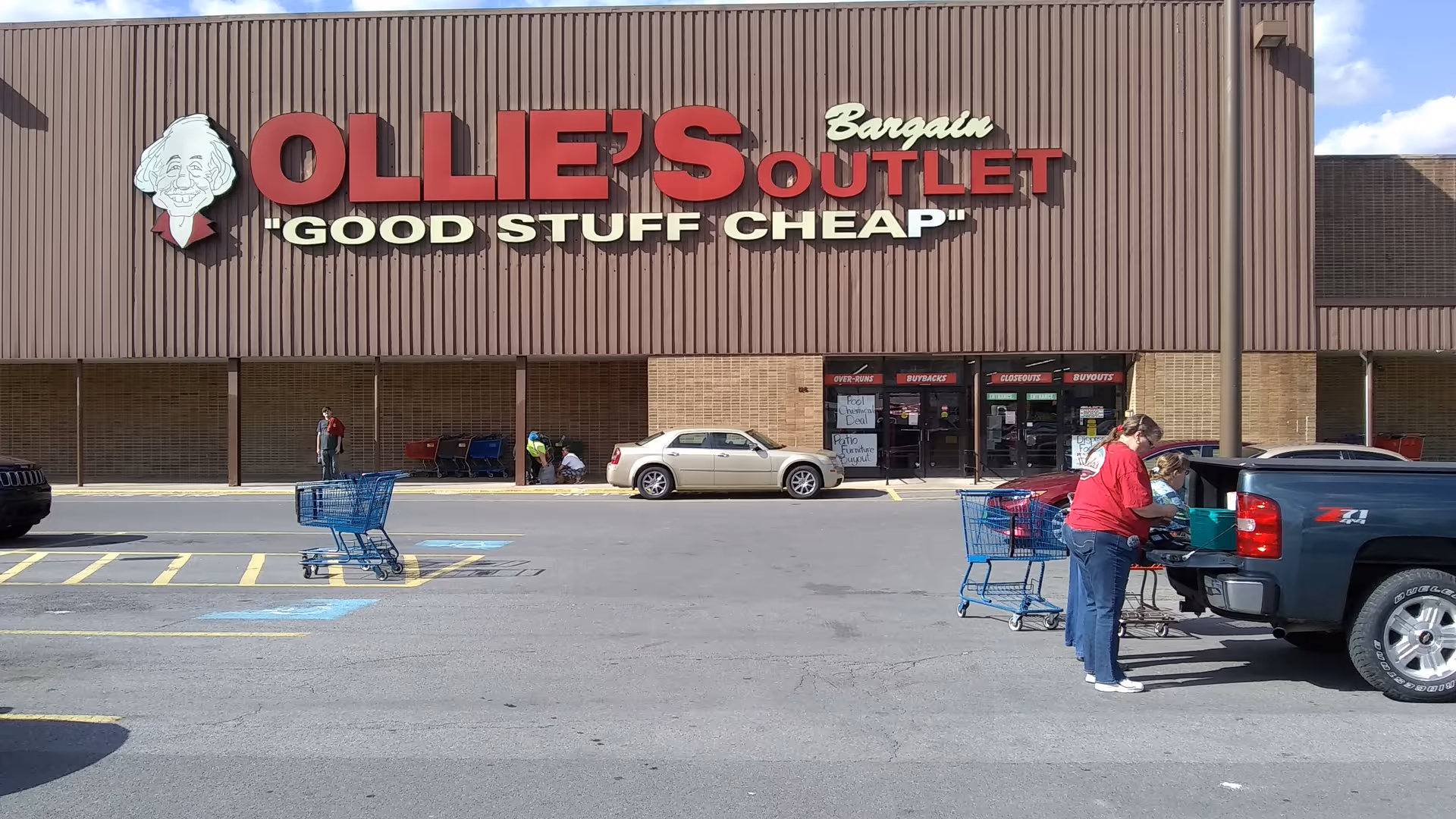 Exterior view of Ollie's Bargain Outlet with shoppers and shopping carts in parking lot.