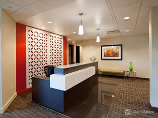 Modern reception desk in a senior living lobby with red geometric accent wall and seating.