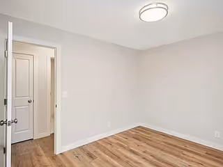 A small empty room with light gray walls, hardwood floor, and an open doorway.