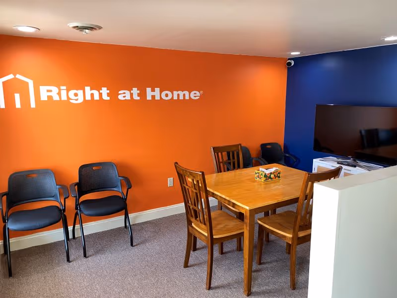 Orange-walled communal dining area with a wooden table, chairs, and a TV.