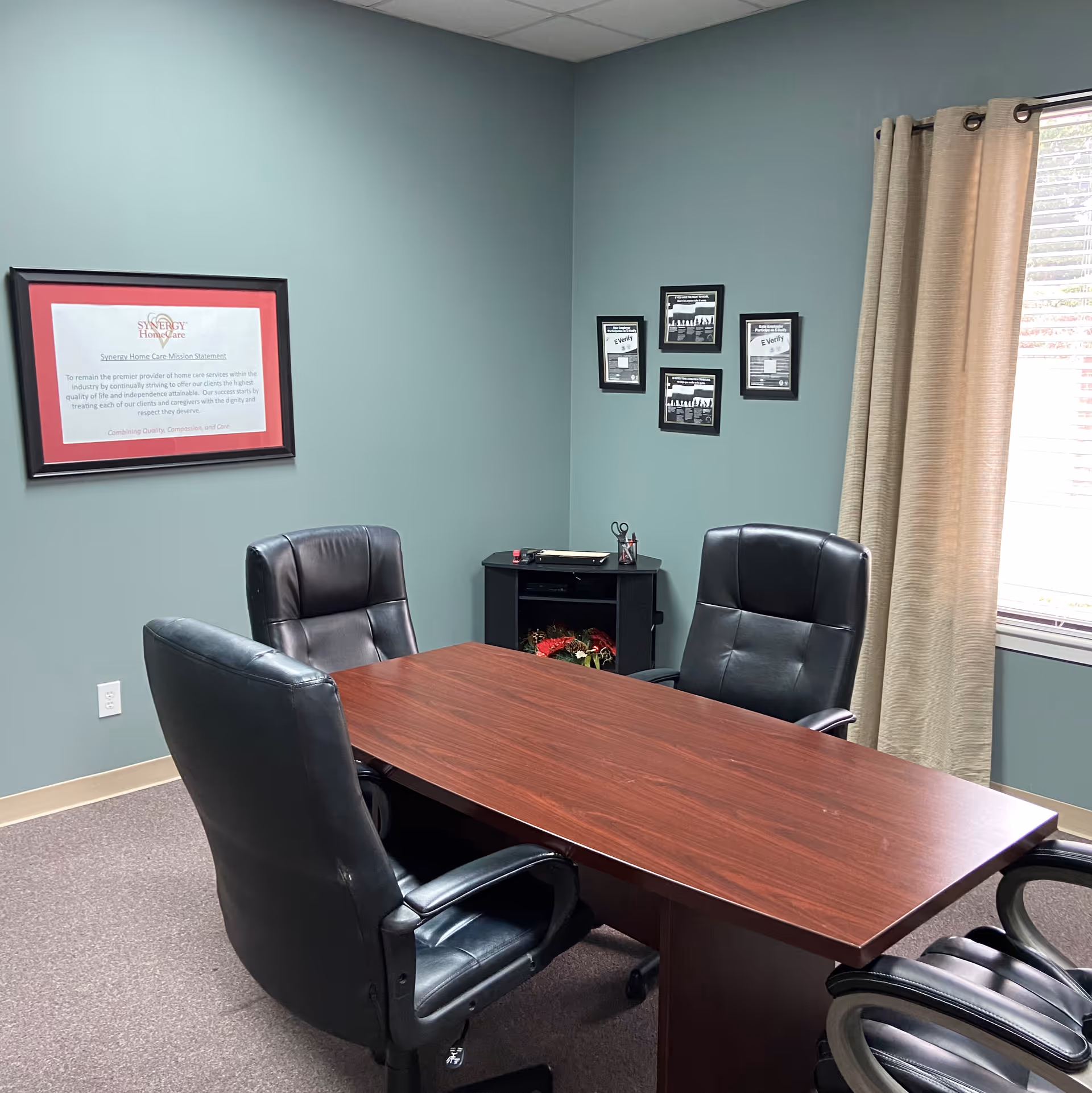 Interior office conference room with a wooden table, black chairs, and framed wall art.
