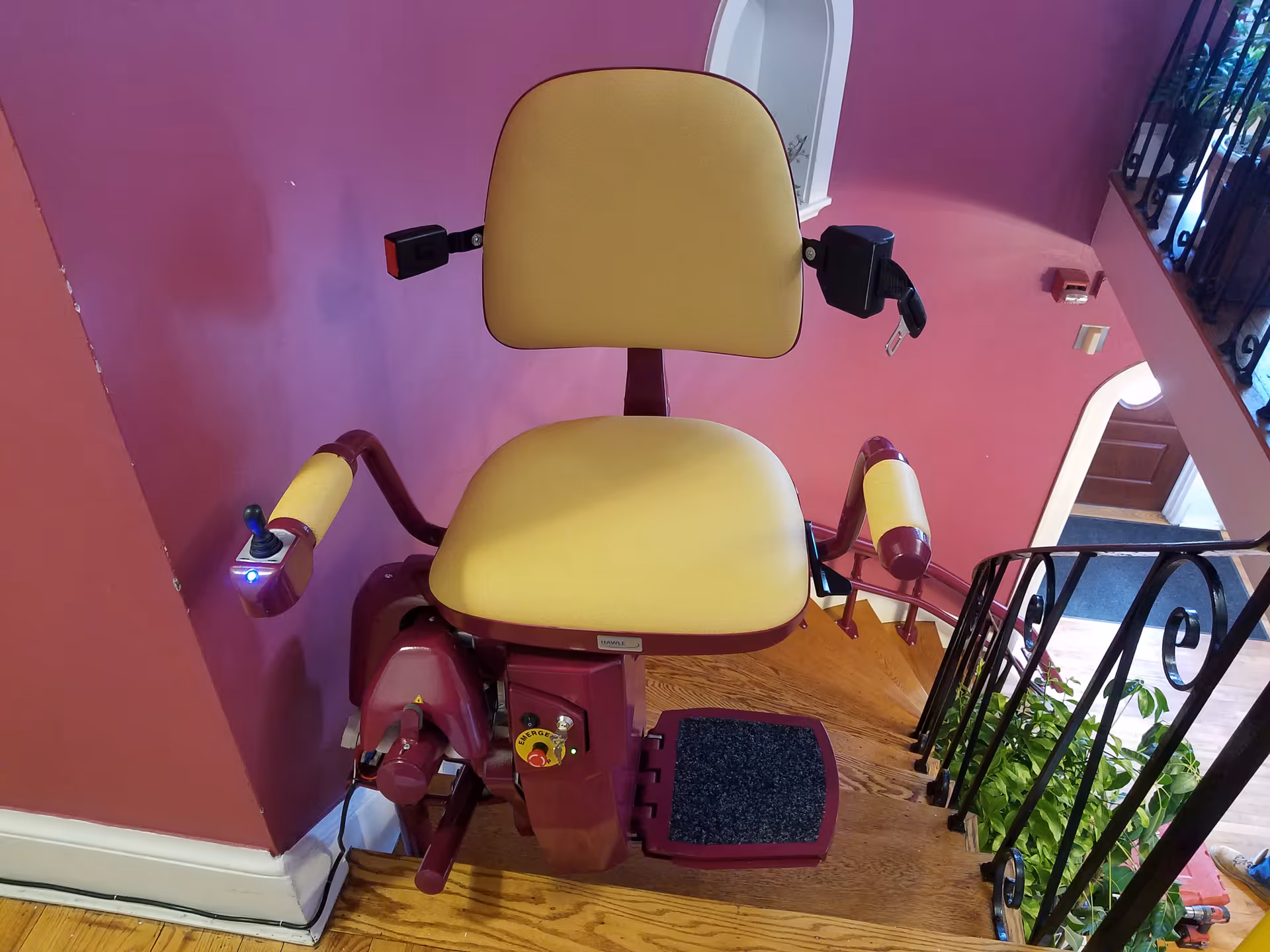 A stairlift chair installed on a staircase with pink walls inside a senior living facility.