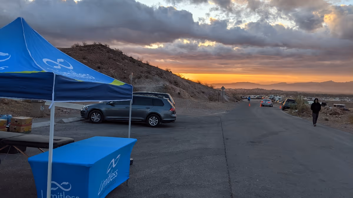 Outdoor road scene with a blue Limitless tent, parked cars, and a person walking at sunset.
