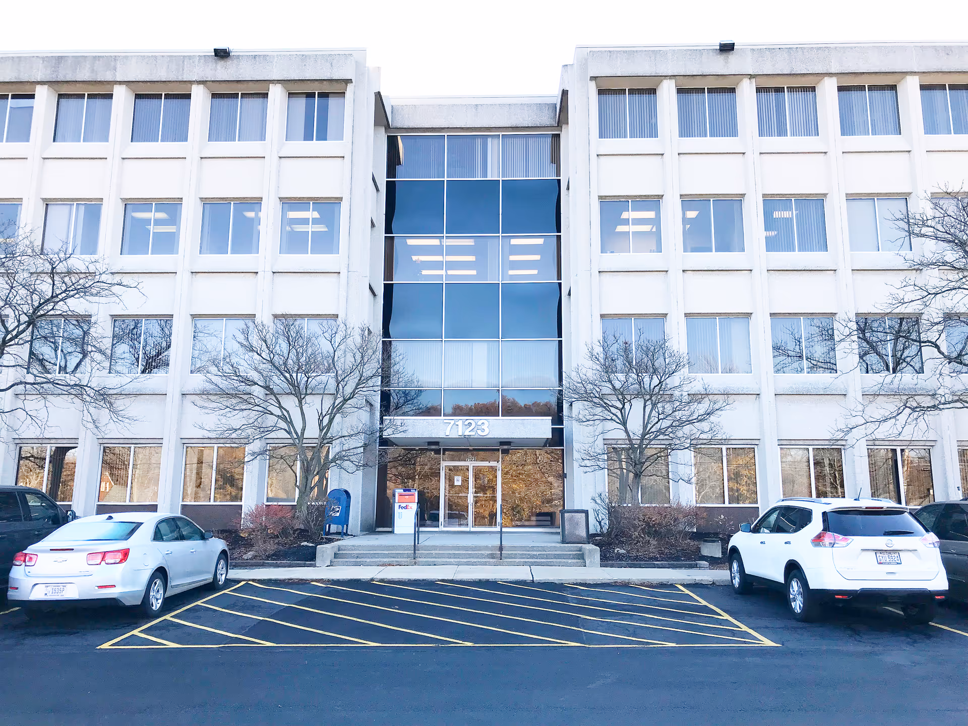Front view of a large light-colored building with a glass central entrance and parking.