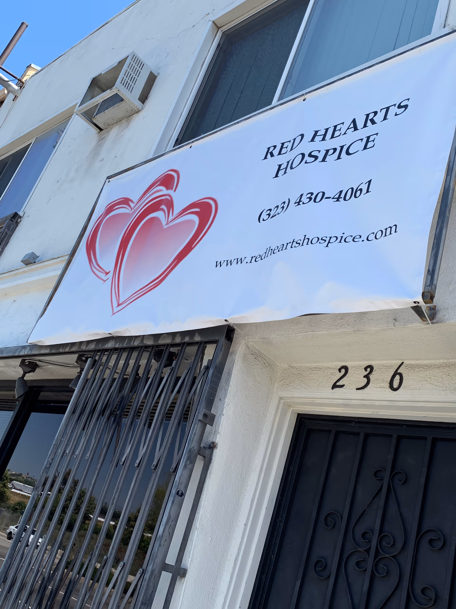 White exterior building with a large Red Hearts Hospice banner above the doorway.