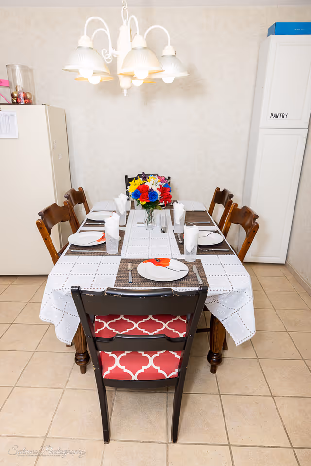A dining table set for six in a bright dining area with a flower centerpiece.