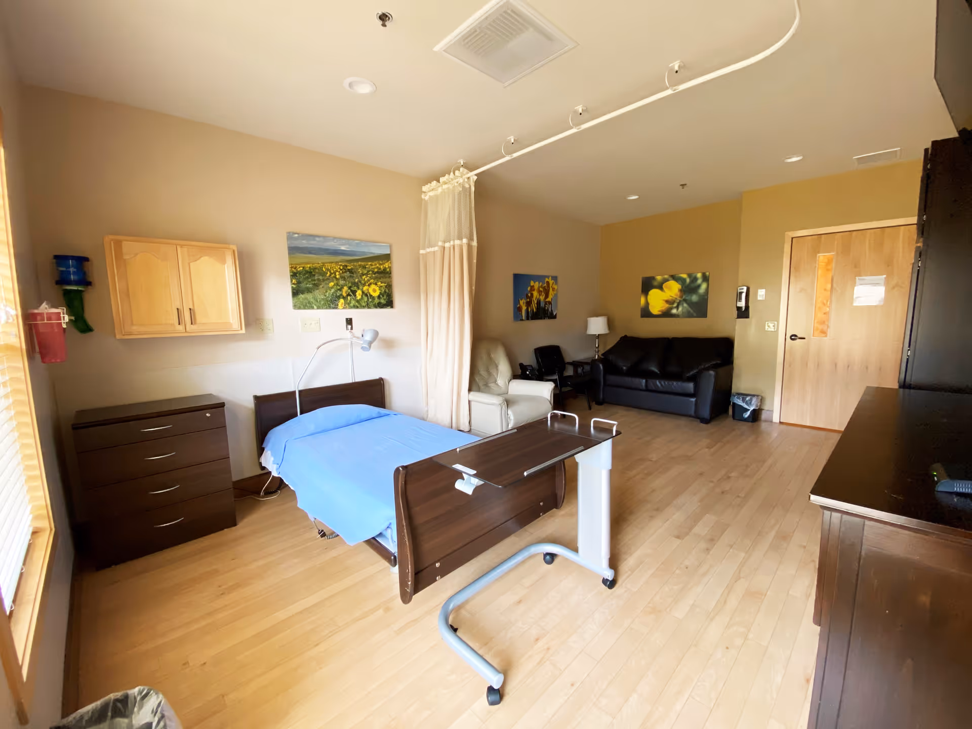 Patient room in a senior facility featuring a bed, dresser, and seating area.