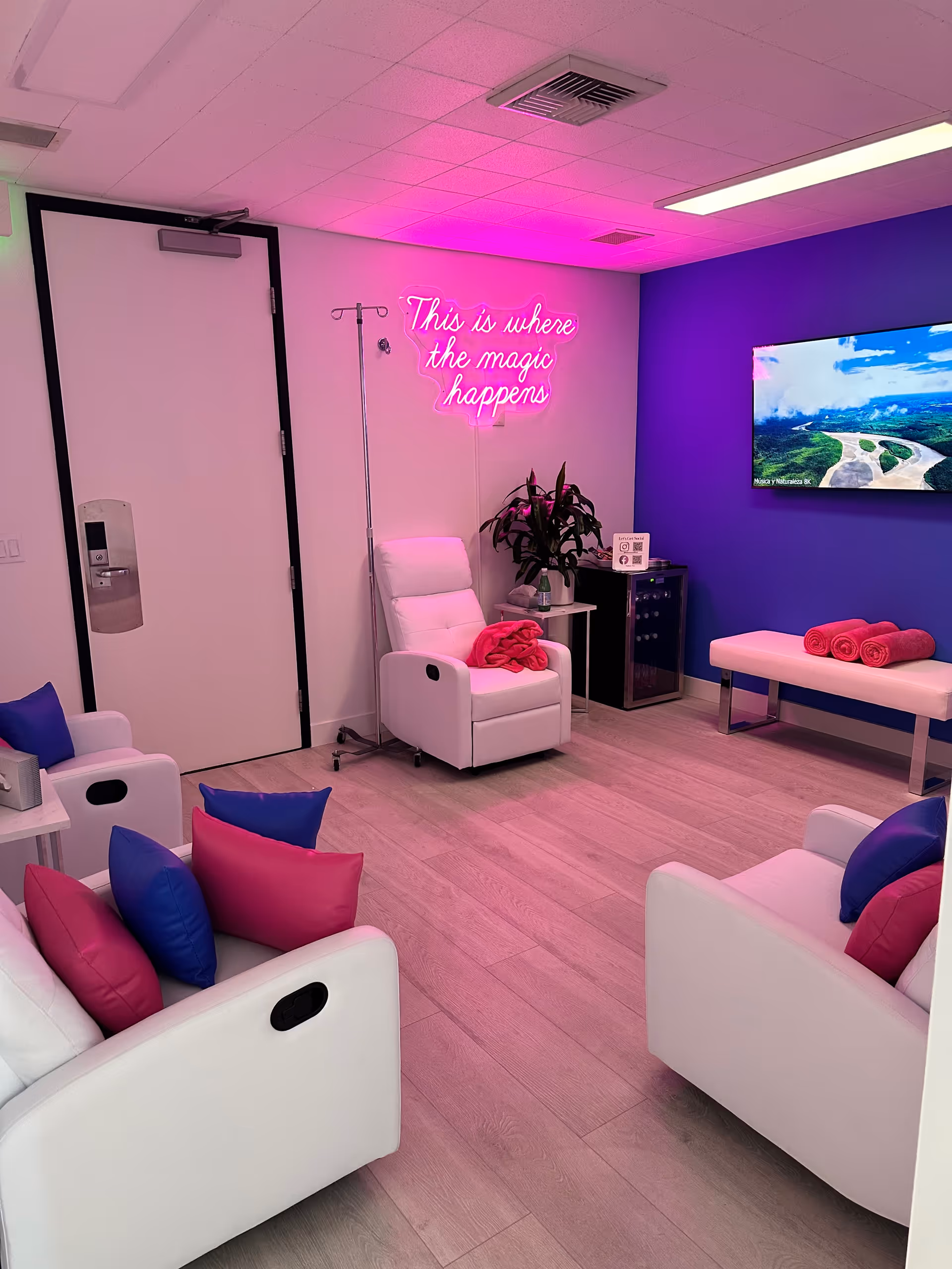 Lounge area with white seating, neon sign, plant, and a wall-mounted TV.