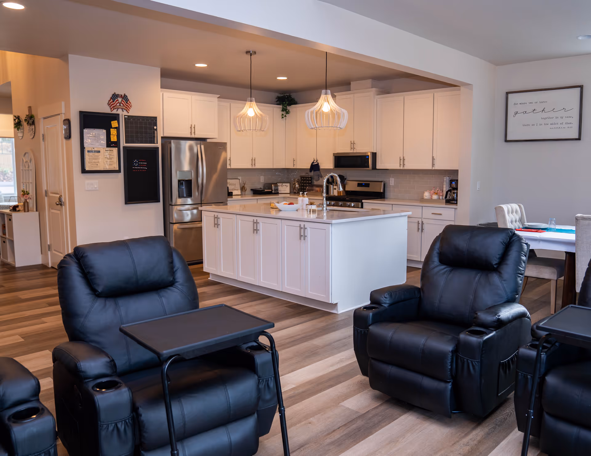 Open living area with white kitchen island, white cabinets, and black leather recliners.