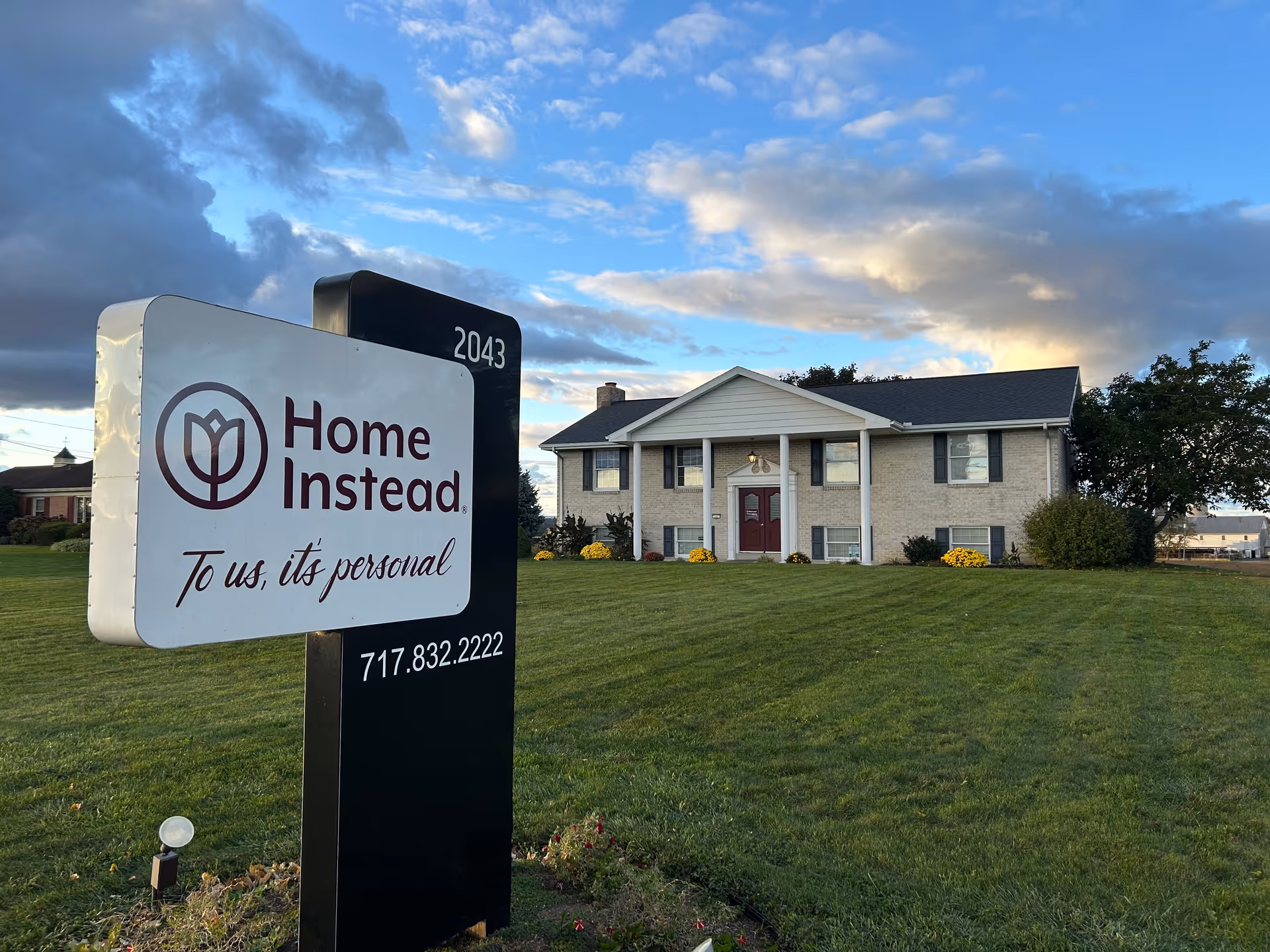 Exterior view of a two-story Home Instead building with a large sign on the lawn.