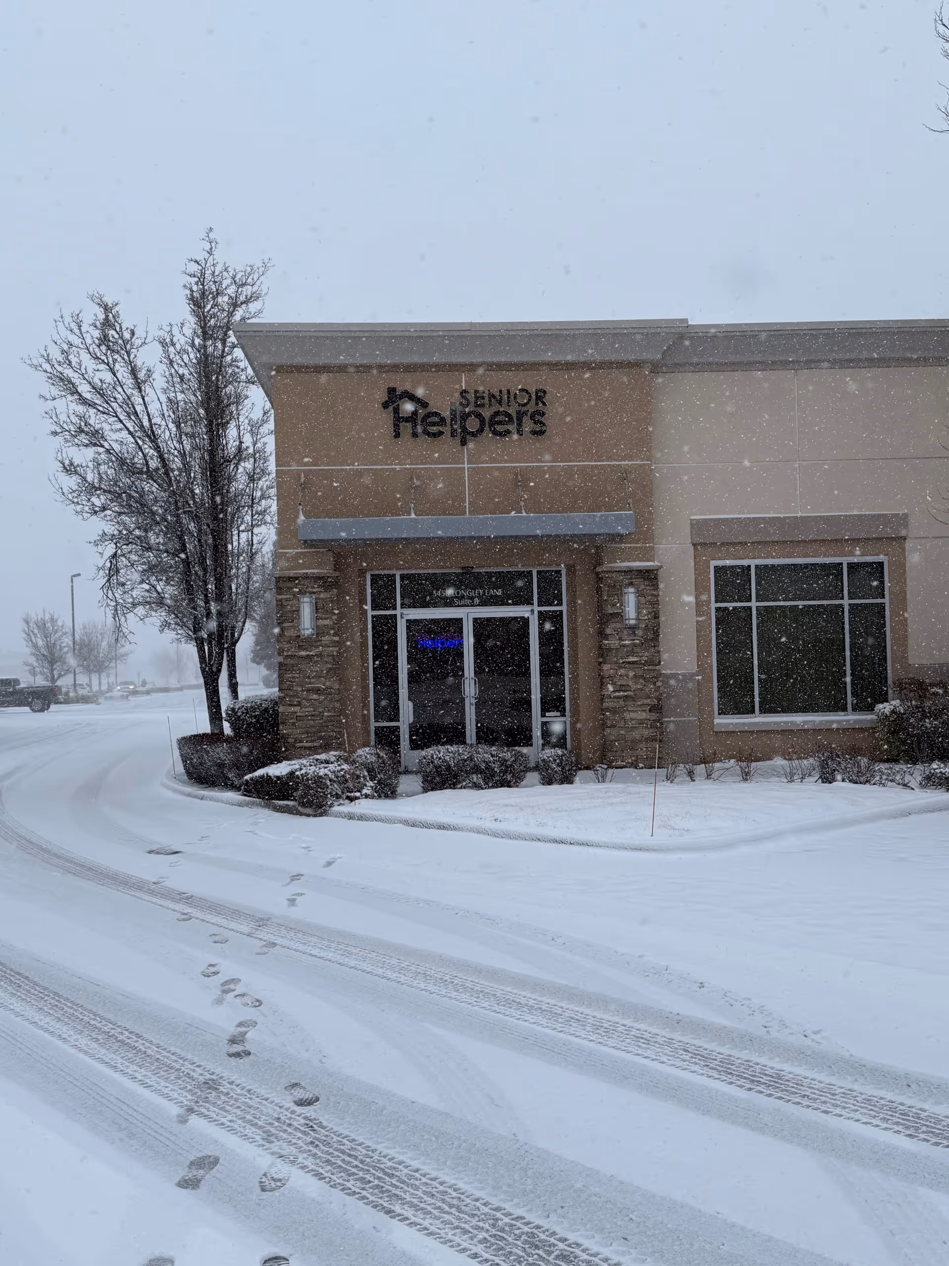 Snowy exterior of the Senior Helpers facility with front doors and a drifted driveway.