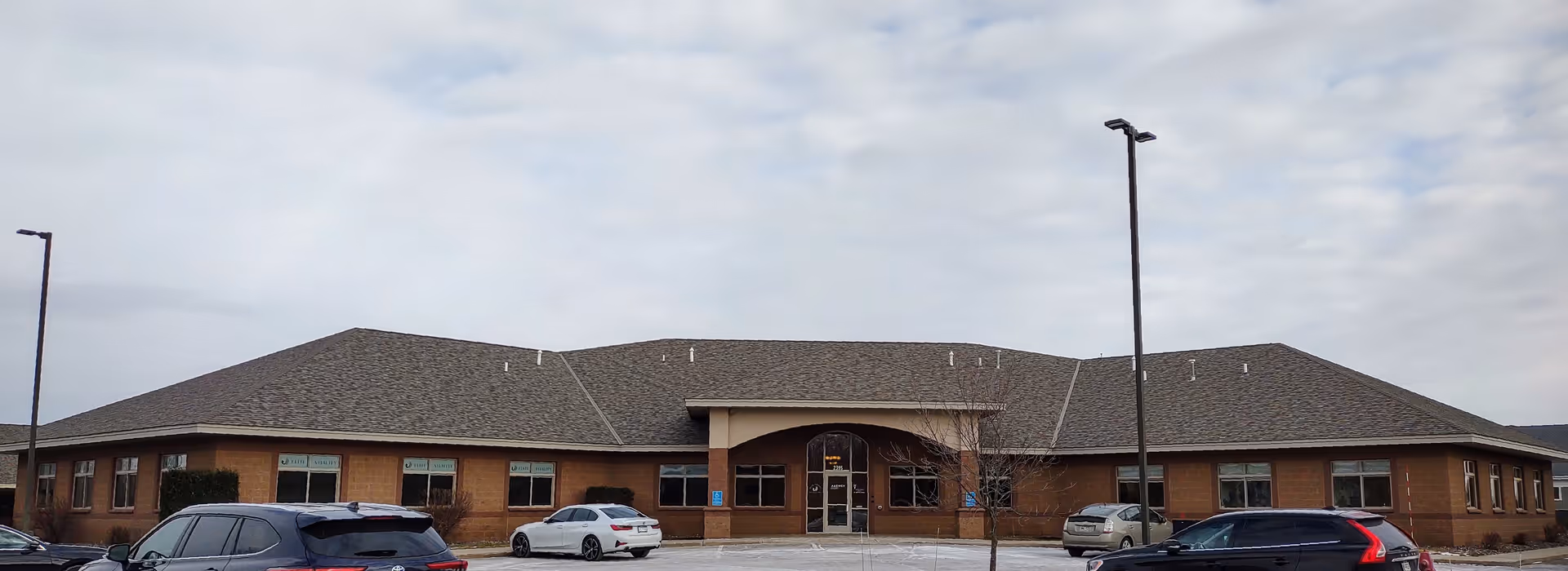 Front exterior view of a one-story brick senior living facility with parked cars.