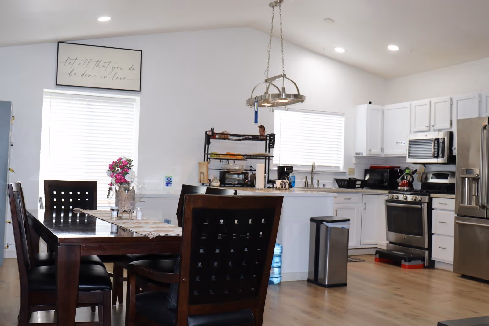 Bright open kitchen and dining area with white cabinets, stainless appliances, and a dark wood table.