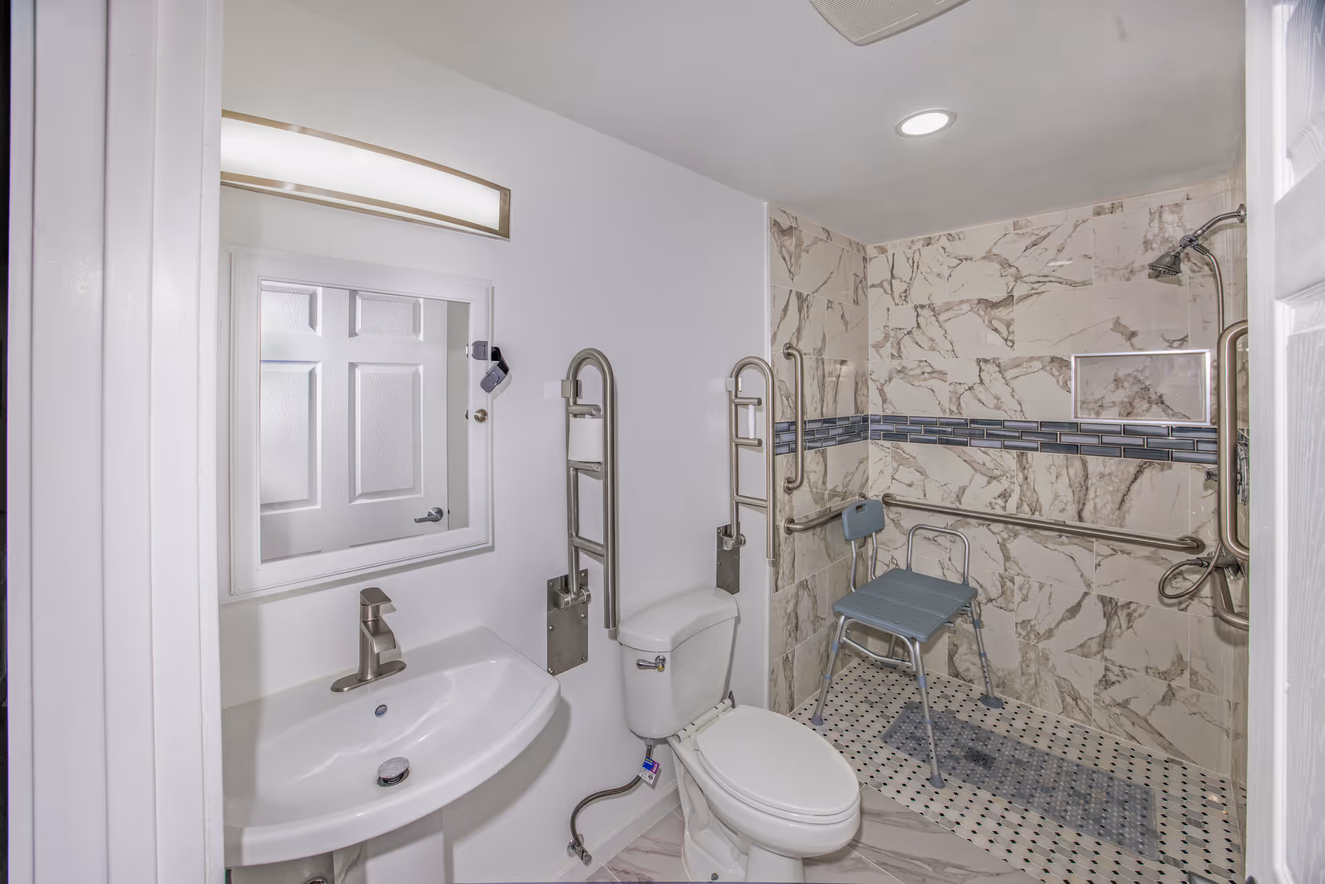 Accessible bathroom in Clover Care Adult Family Home with chair, grab bars, sink, and toilet.