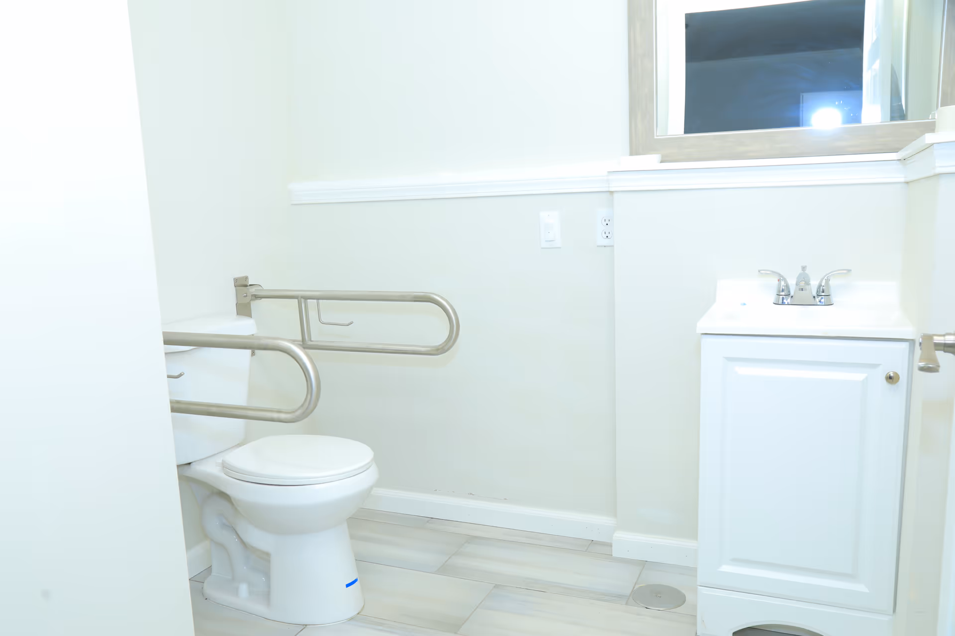Accessible bathroom with toilet, grab bars, and sink in a light-colored room.
