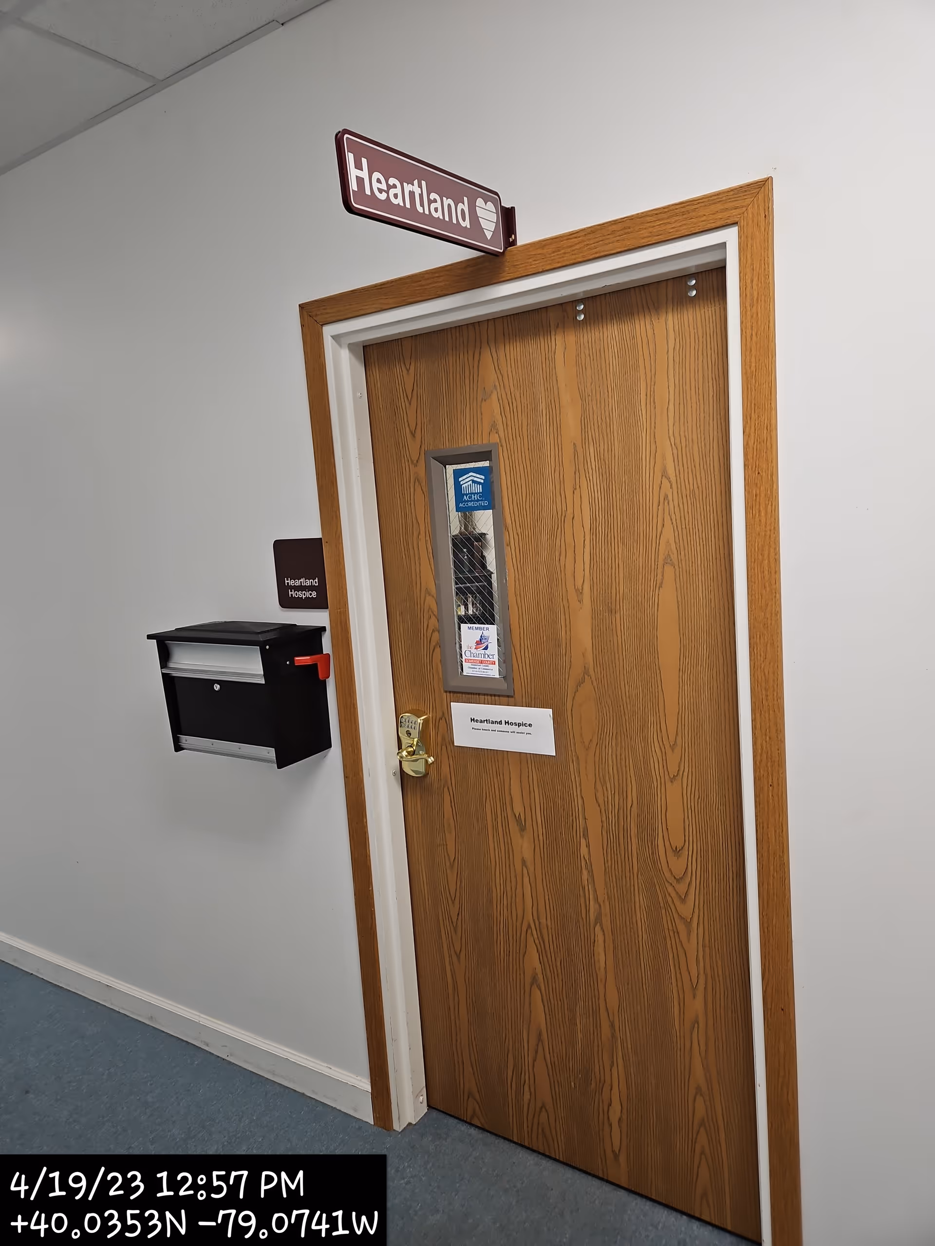 Interior hallway with a wooden door labeled Heartland Hospice and a mailbox on the wall nearby.