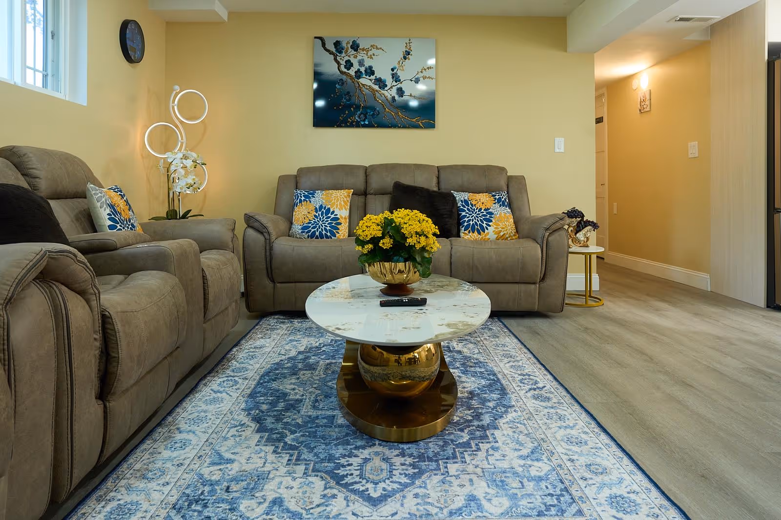 Cozy living room with beige couches, pillows, and a yellow-flower centerpiece on a marble coffee table.