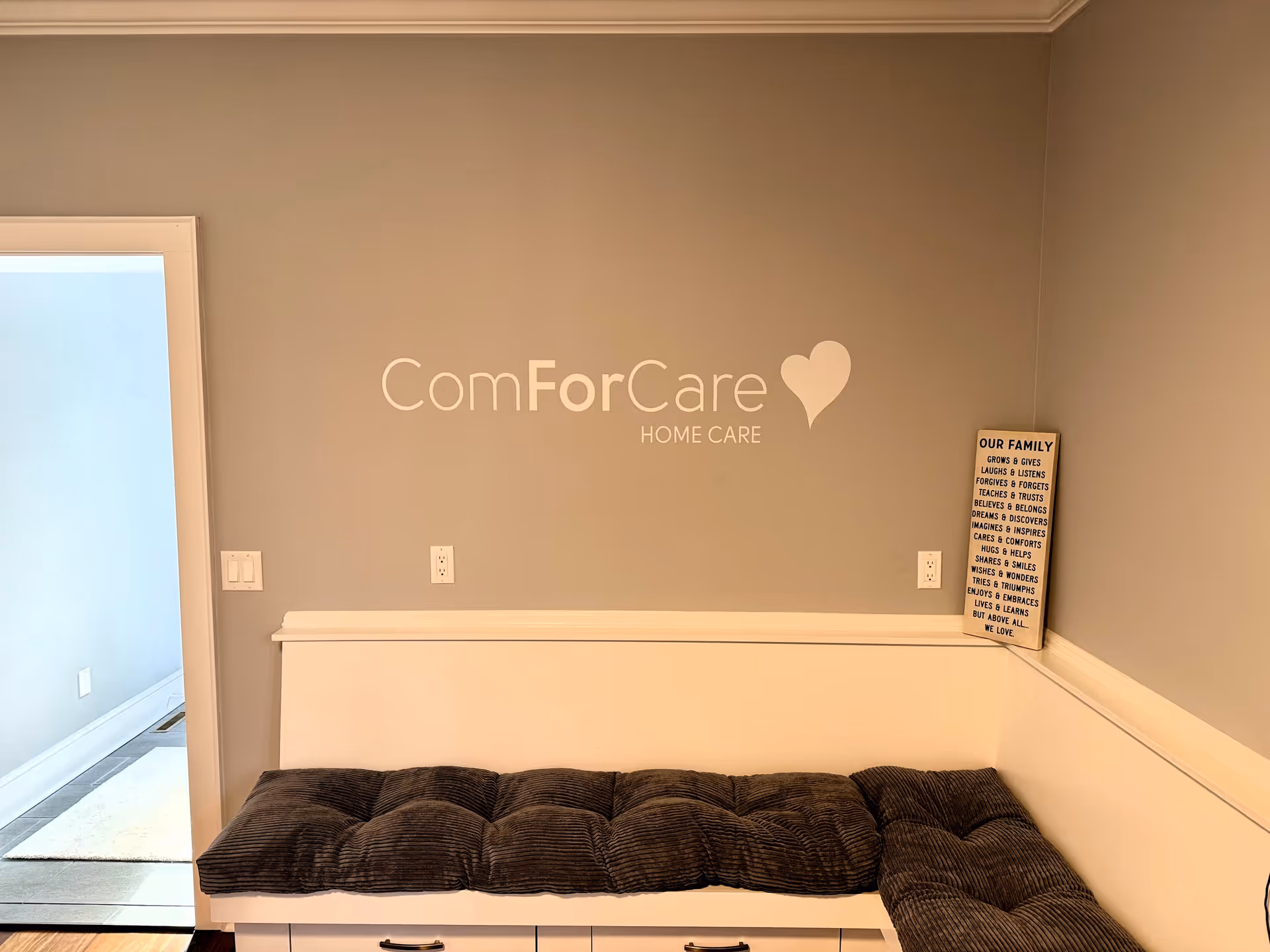 Interior room with a gray wall, cushioned bench, and ComForCare Home Care sign.