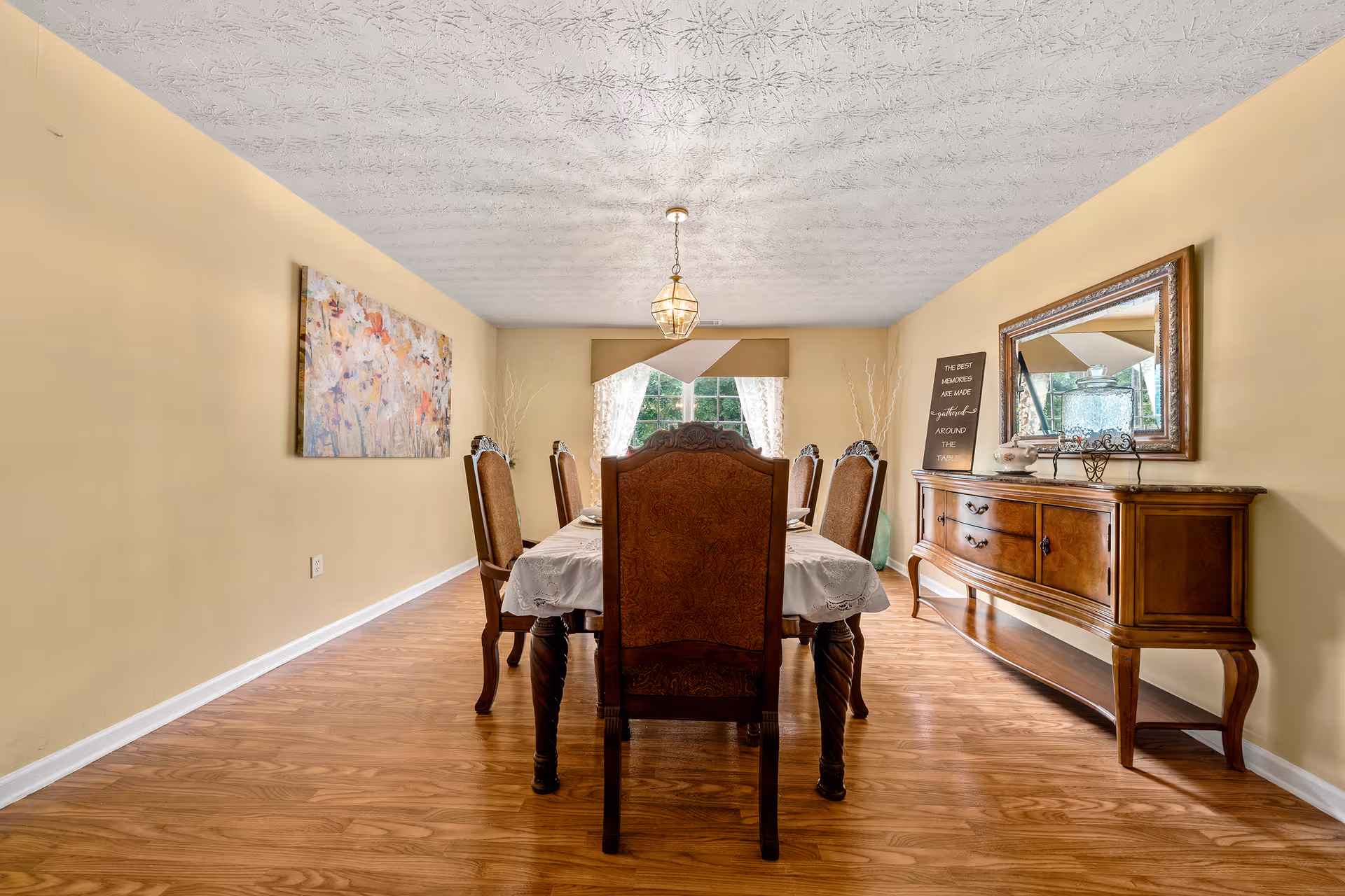 A dining room with a wooden table, ornate chairs, sideboard, chandelier, and warm yellow walls.