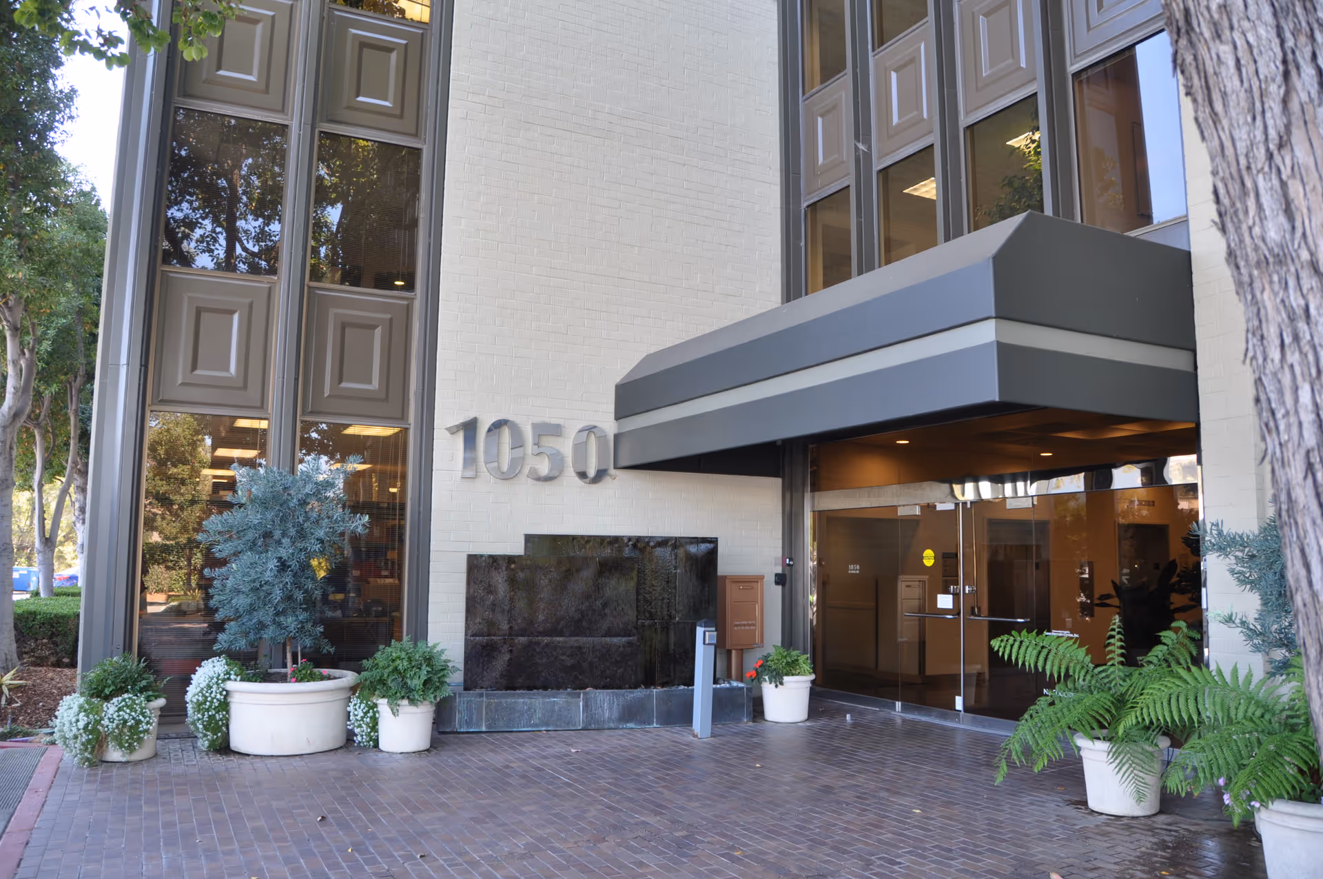 Senior living facility entrance with glass doors, canopy, and potted plants at address 1050.