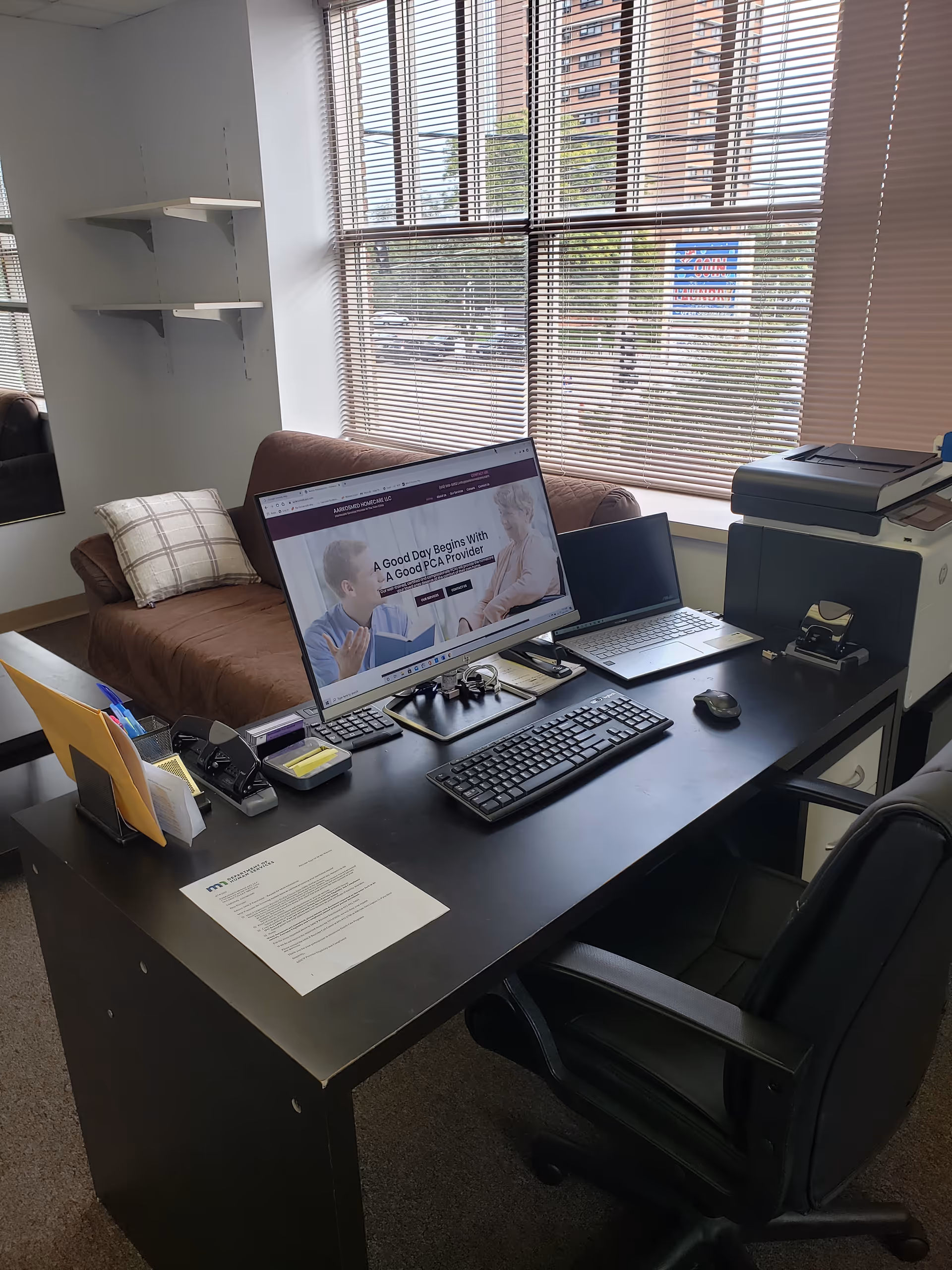 Office workspace with computer, printer, and window blinds in a senior living facility.