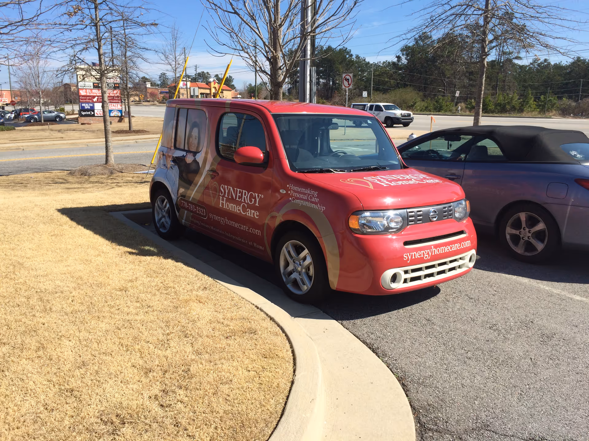 Red Synergy HomeCare van parked in a lot beside a purple convertible.