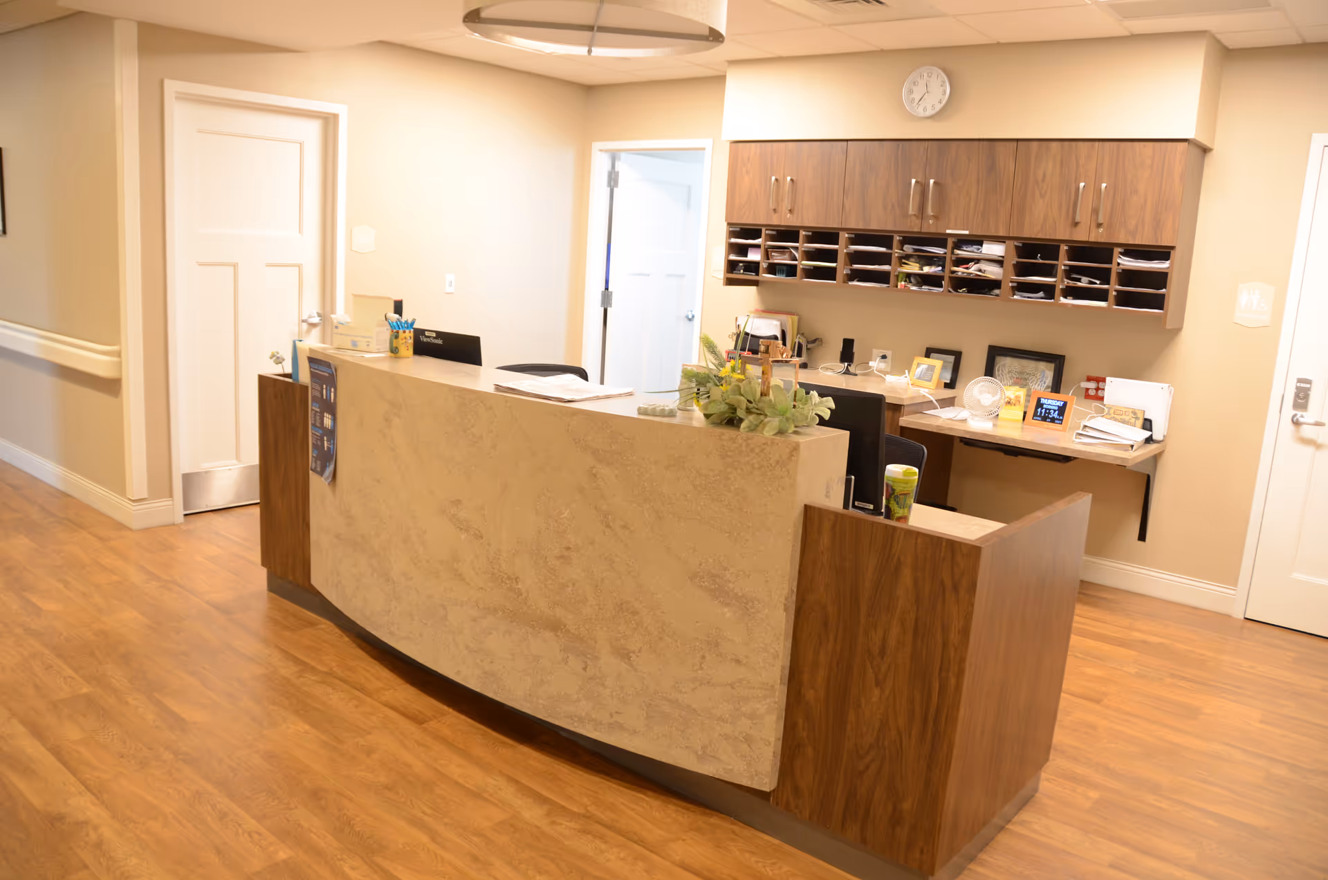 Reception desk in a warmly lit facility lobby with wood cabinets, a plant, and organized paperwork.