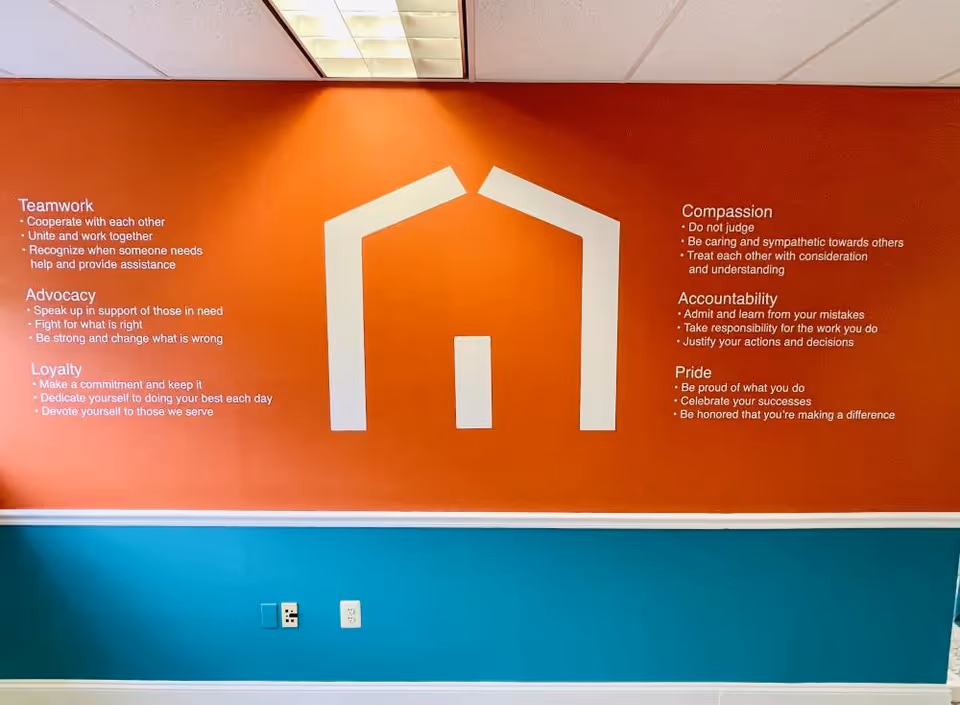 Orange wall mural with a white house icon and bullet-point text in a teal-trimmed interior hall.