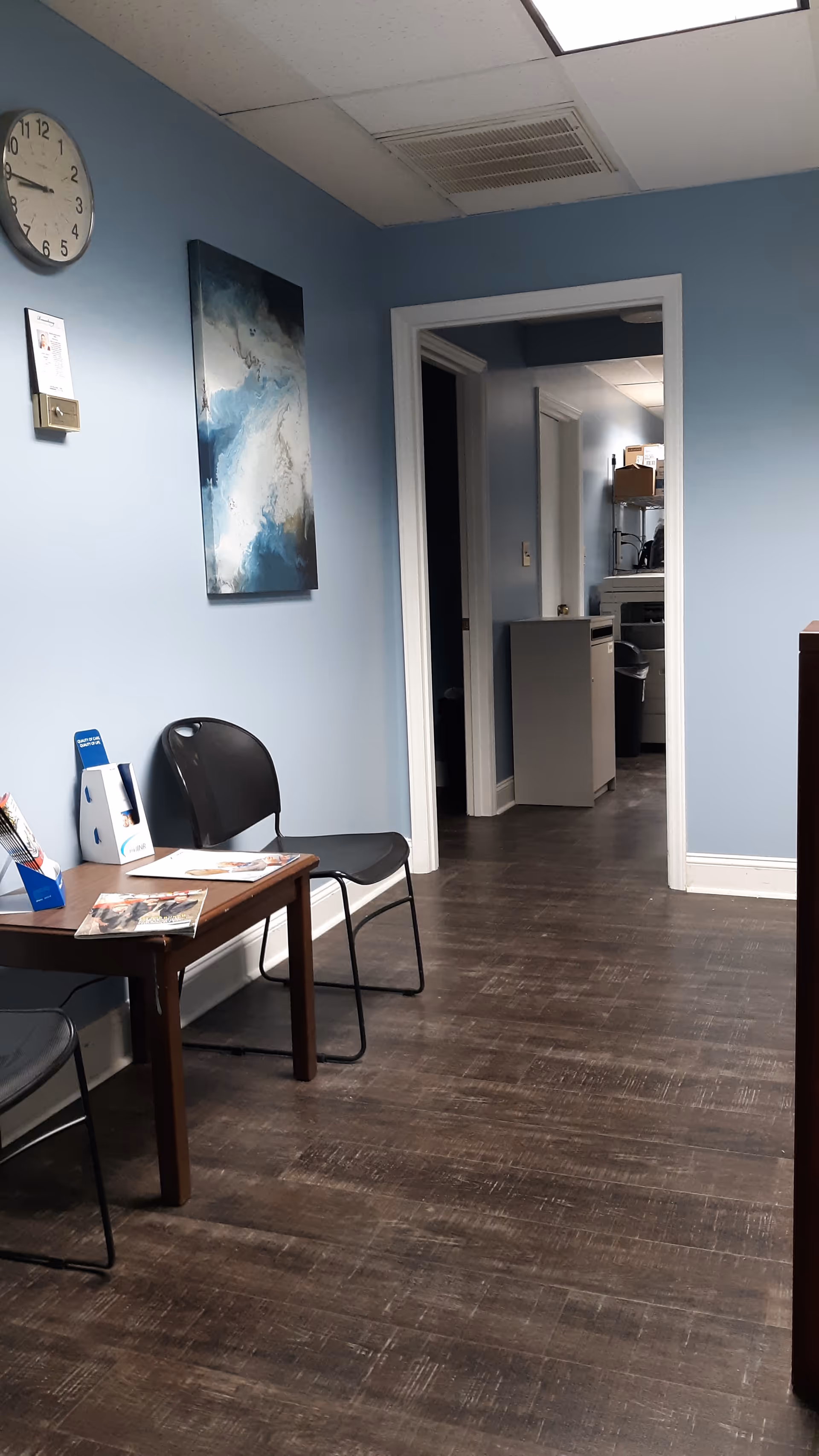 Blue-walled interior hallway with a small waiting area, table, chairs, and wall art.