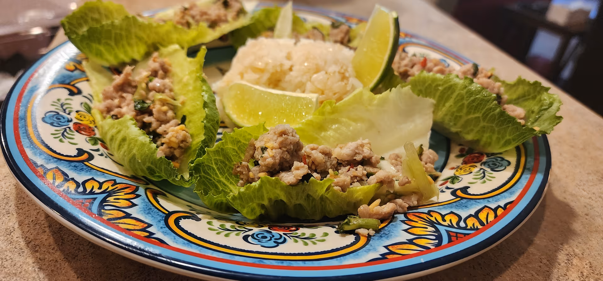 Colorful plate of lettuce wraps with lime wedges in a dining area.