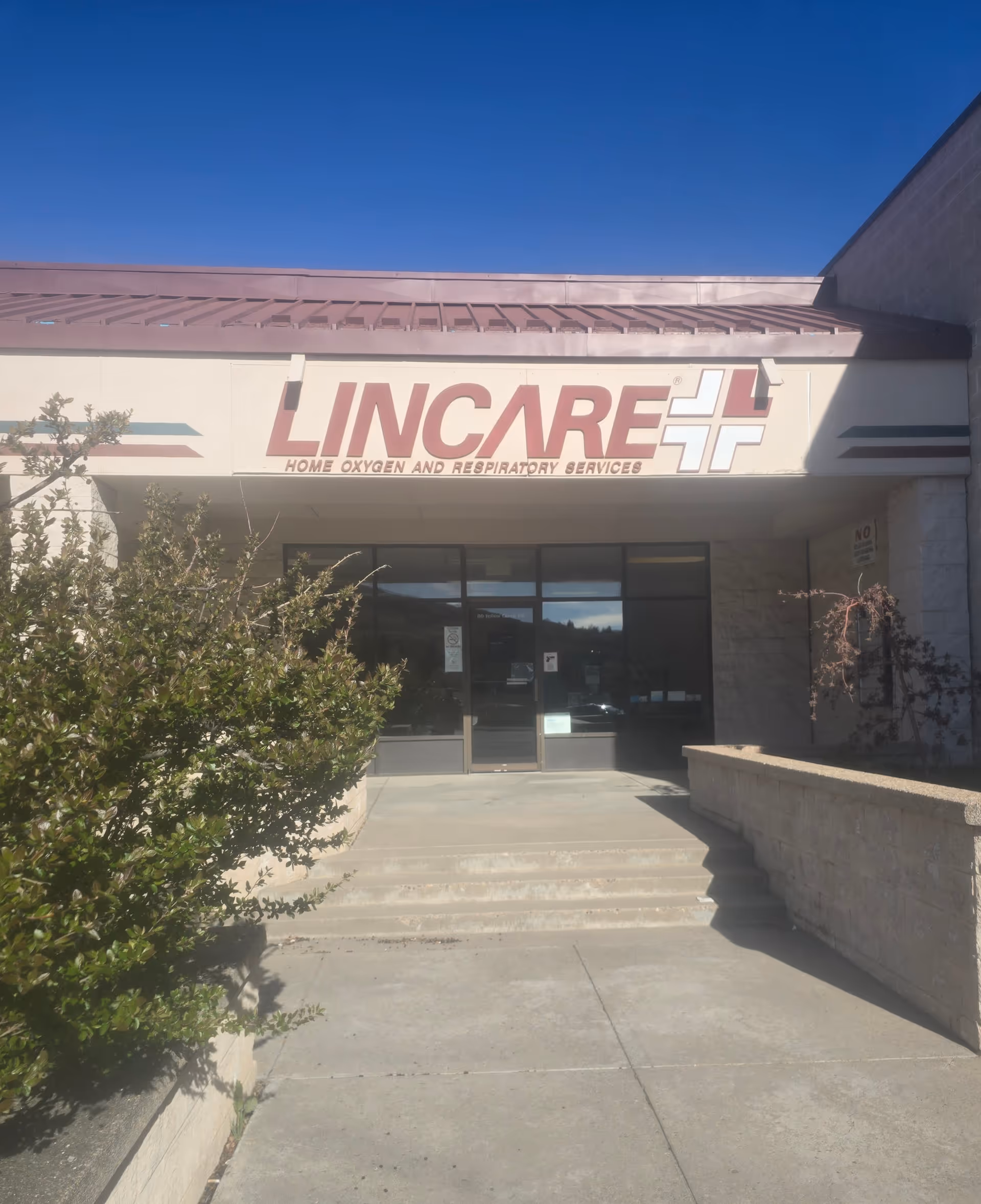 Front exterior of a LINCARE facility with a large sign, glass doors, and concrete steps.