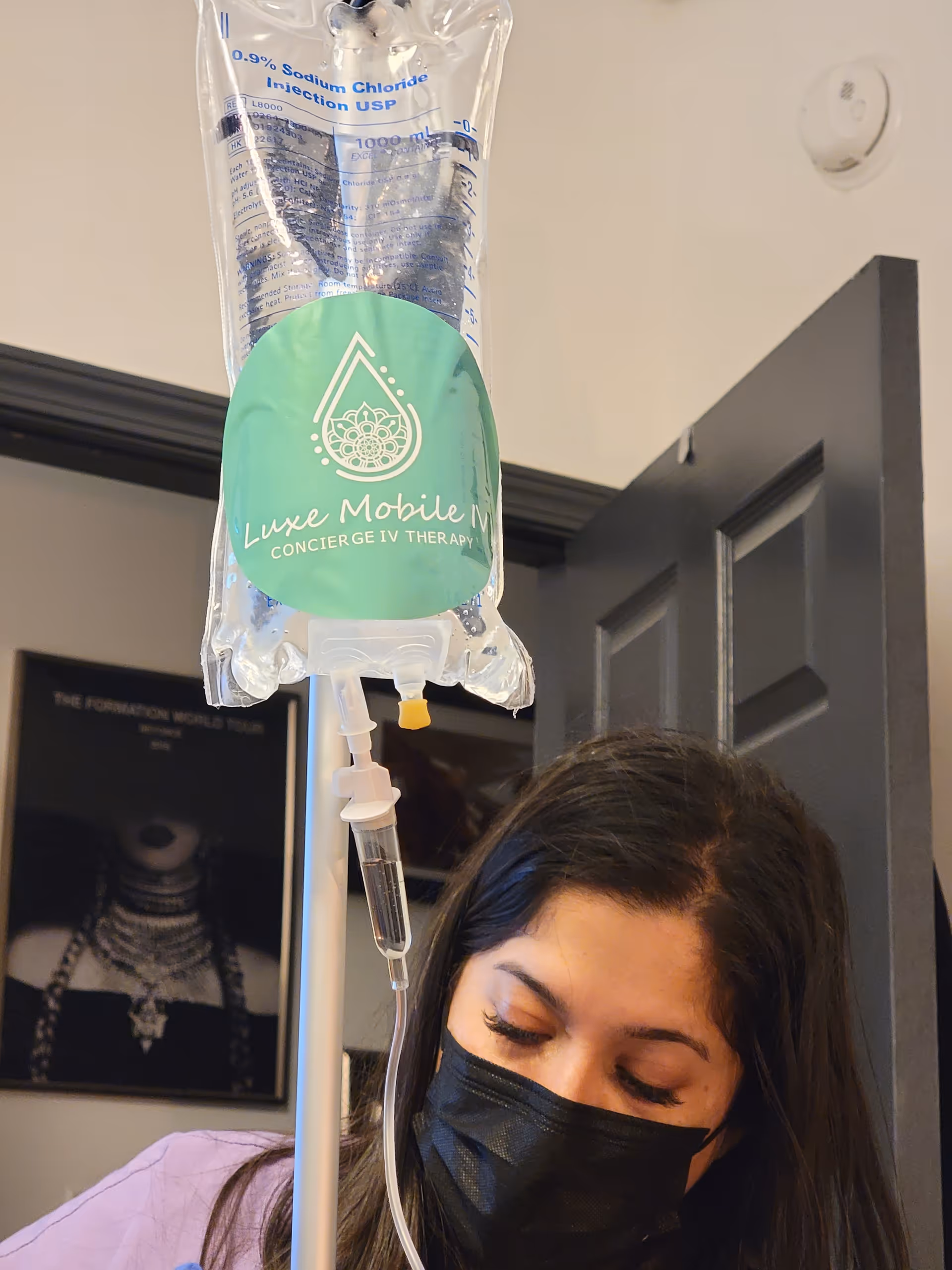 IV therapy bag labeled Luxe Mobile IV Houston hangs near a masked caregiver inside a facility