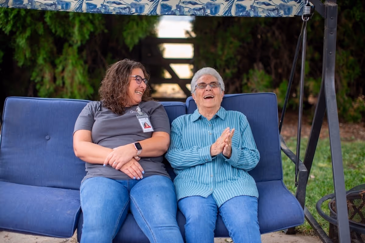 Two women sit on a blue outdoor swing, smiling together.