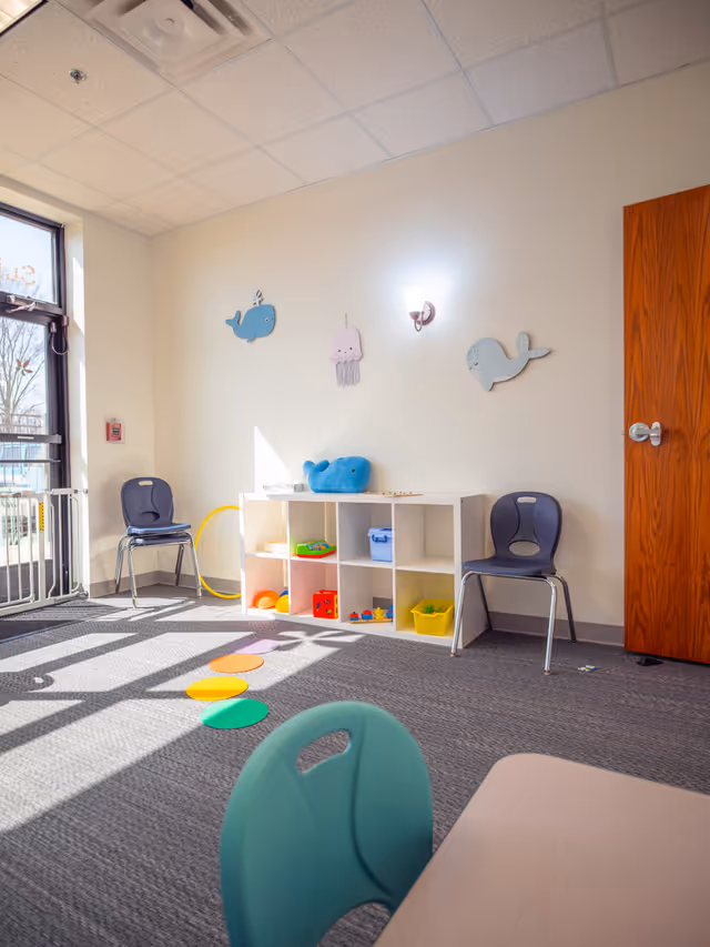 Bright children's play area with cubby shelves, chairs, and colorful mats.