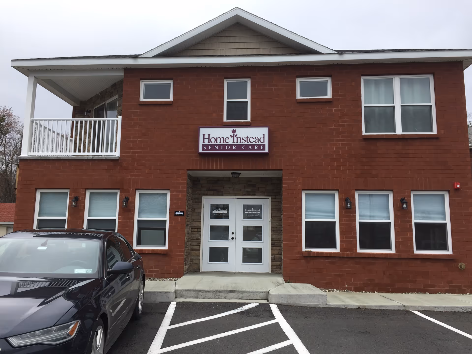 Red brick Home Instead senior care building with entrance and parked car.