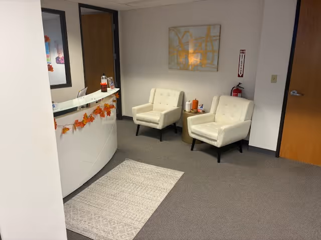 Reception area with white chairs, a curved front desk, and autumn-themed decorations.