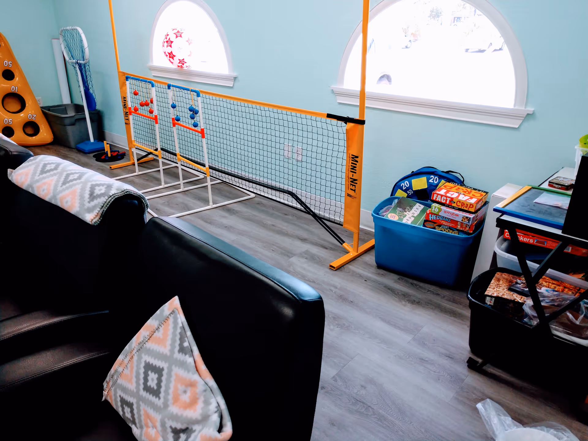 Colorful living room with sofa, patterned pillows, and a game area with nets and board games.