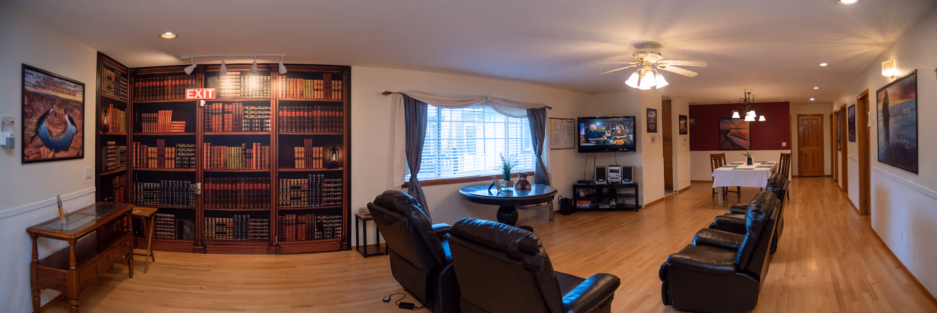 A spacious senior living lounge with leather recliners, a wall bookshelf, and a TV.