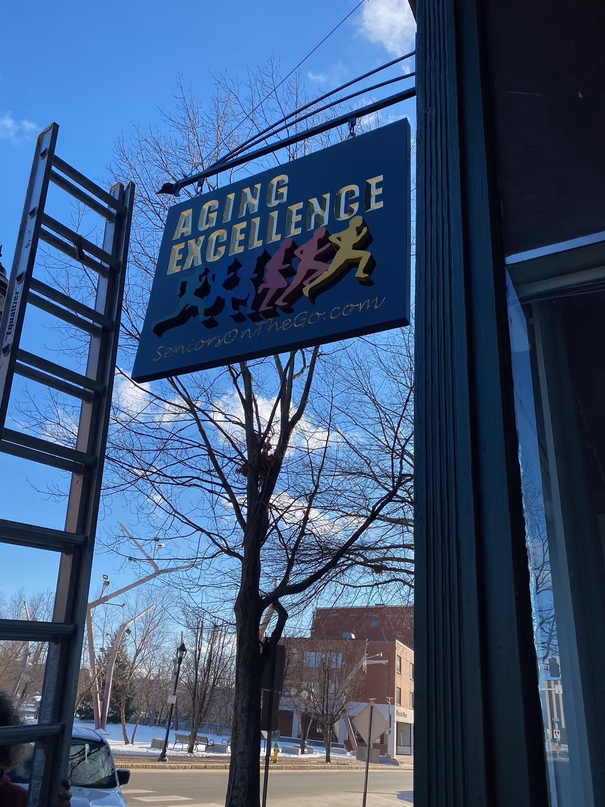 Outdoor Aging Excellence sign hangs beside a building on a clear day