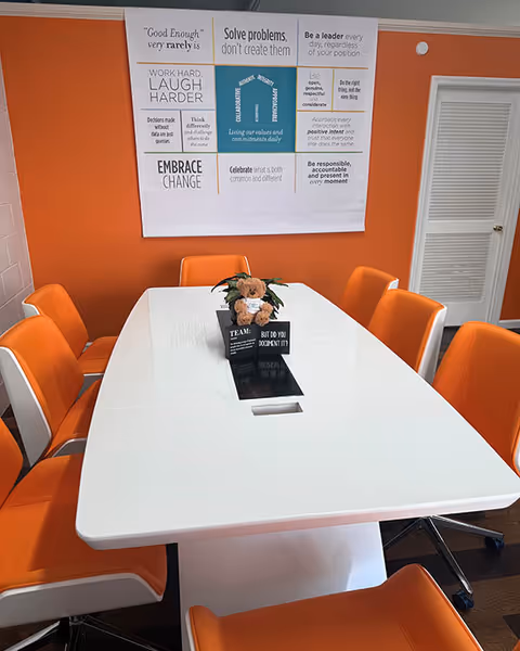 Orange chairs surround a white table with a flower centerpiece in a bright room with posters.