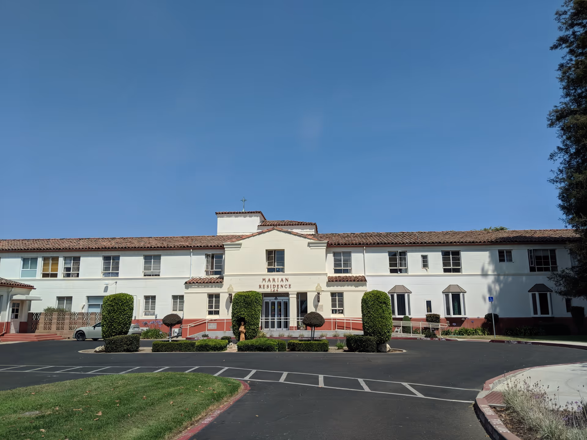 Front view of Marian Residence, a white two-story building with a red tile roof and landscaping.