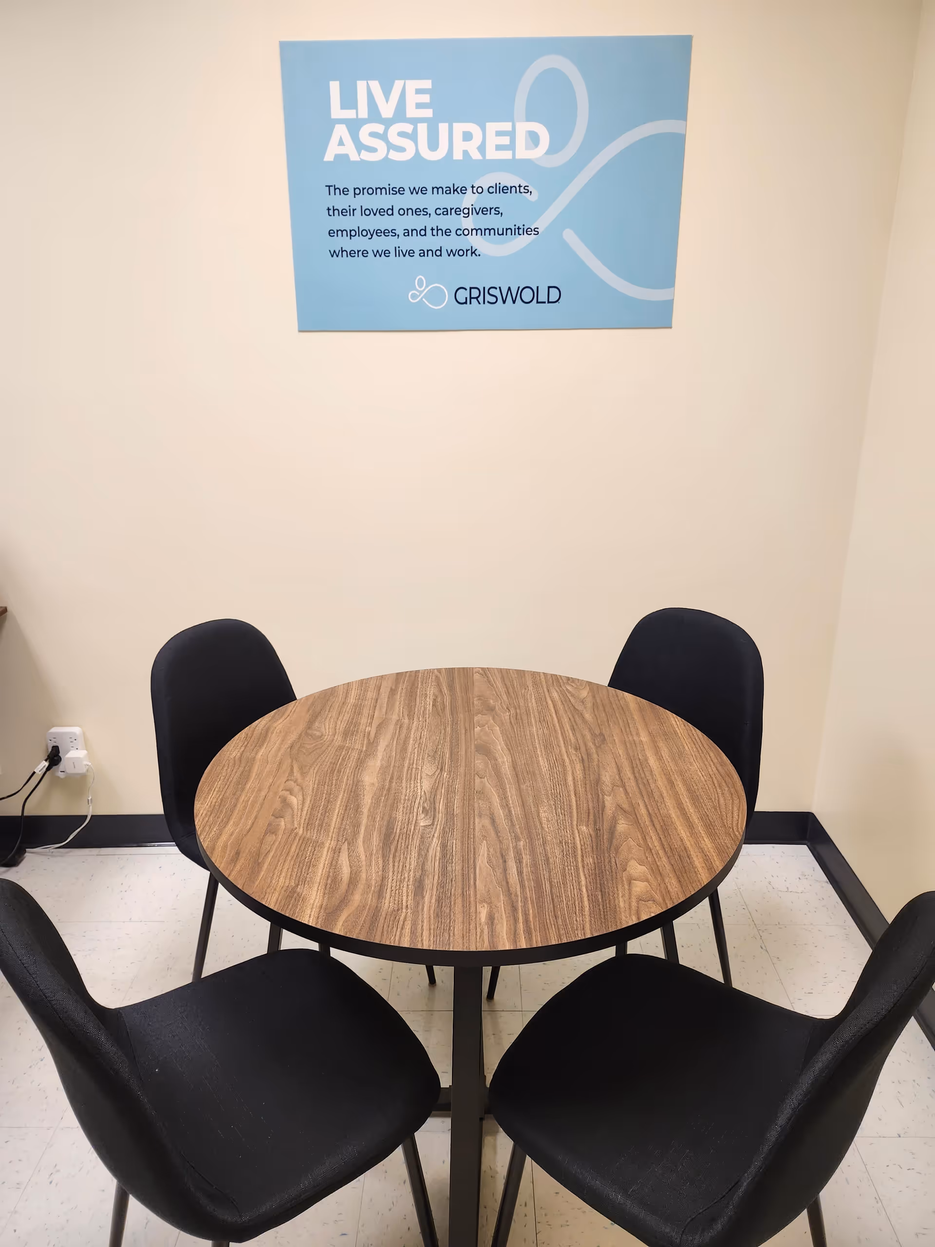 Round wooden table with four black chairs under a blue Griswold poster.